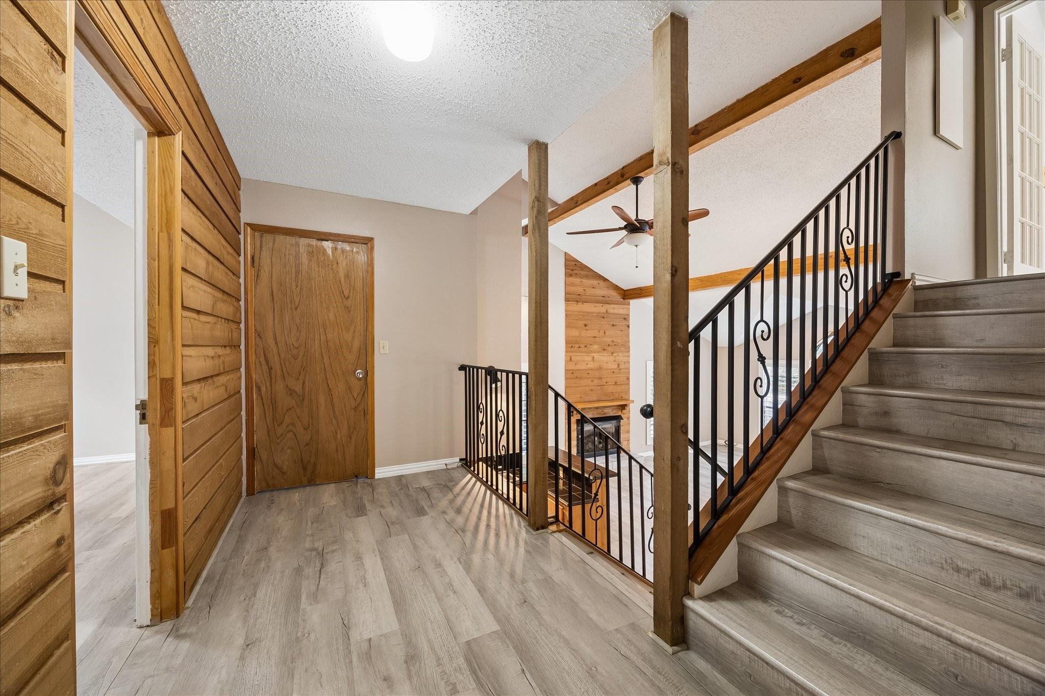 Entry hall with a broad staircase, black iron railings, exposed wooden beams, and wood-paneled walls.