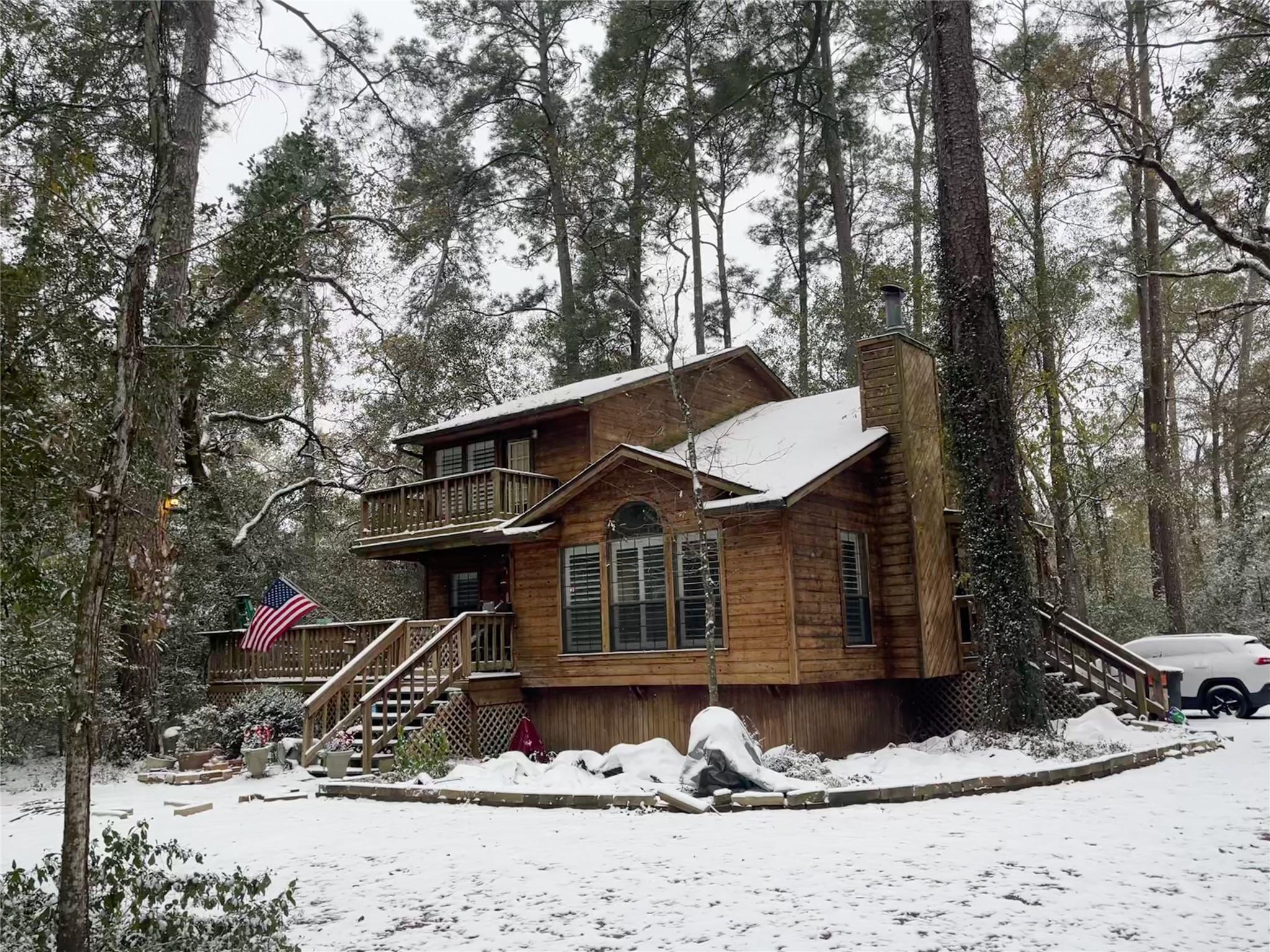 Wood-sided two-story home with decks among snowy trees, with an American flag on the lower deck.