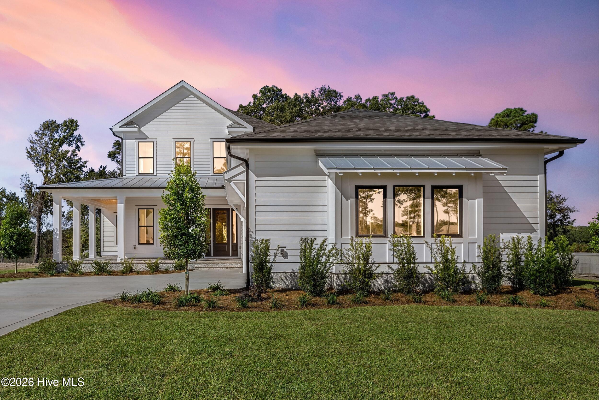 White two-story house with a covered porch and metal window awning beneath a pink dusk sky.