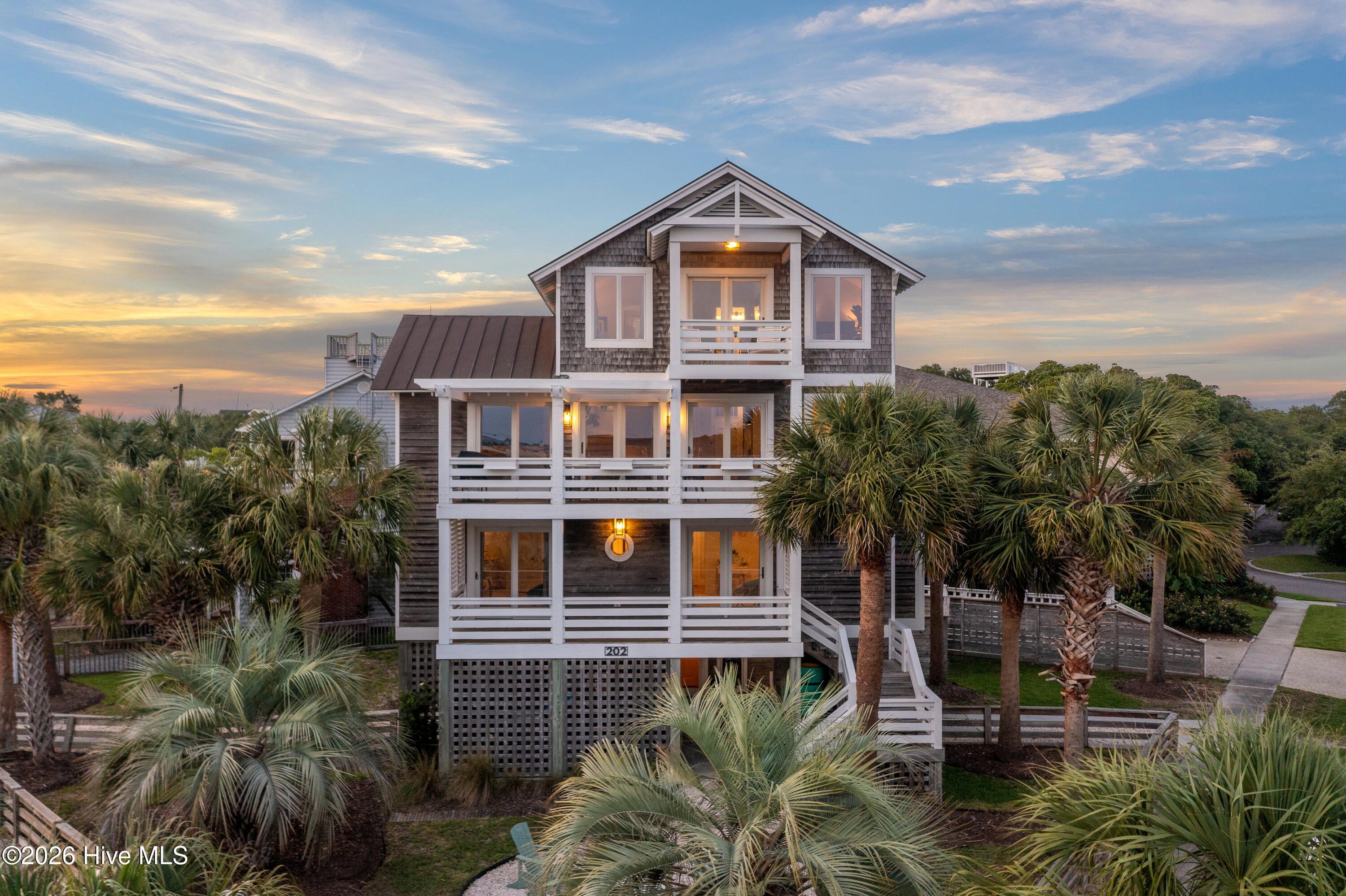 Coastal-style home with white balconies and palm trees, warmly lit at dusk.