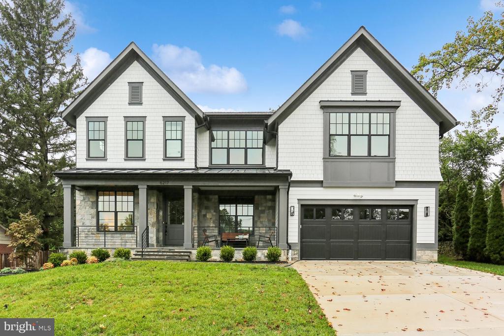 White two-story home with a stone-accented porch, large windows, and an attached two-car garage.