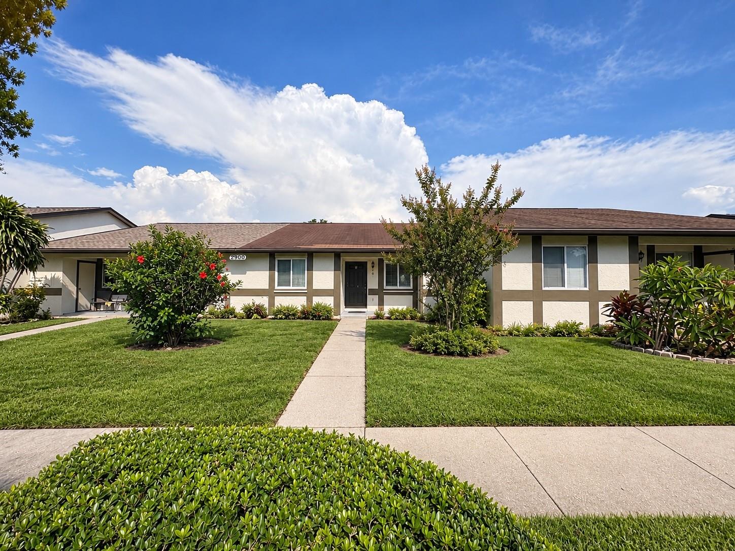 Single-story cream-and-brown home with a landscaped lawn and walkway leading to the front door.