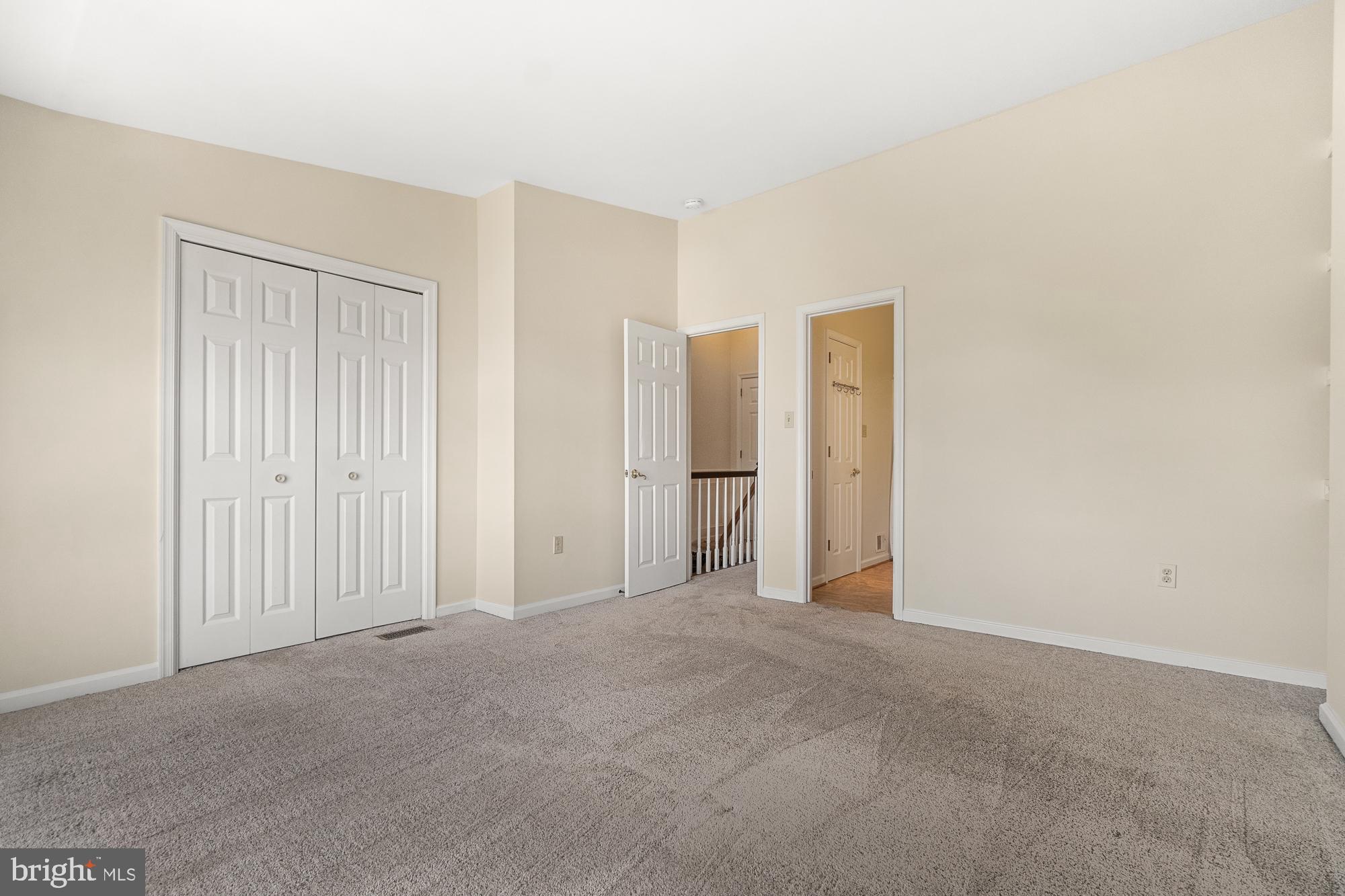 Empty carpeted bedroom with a double-door closet and open doorways to the hall.