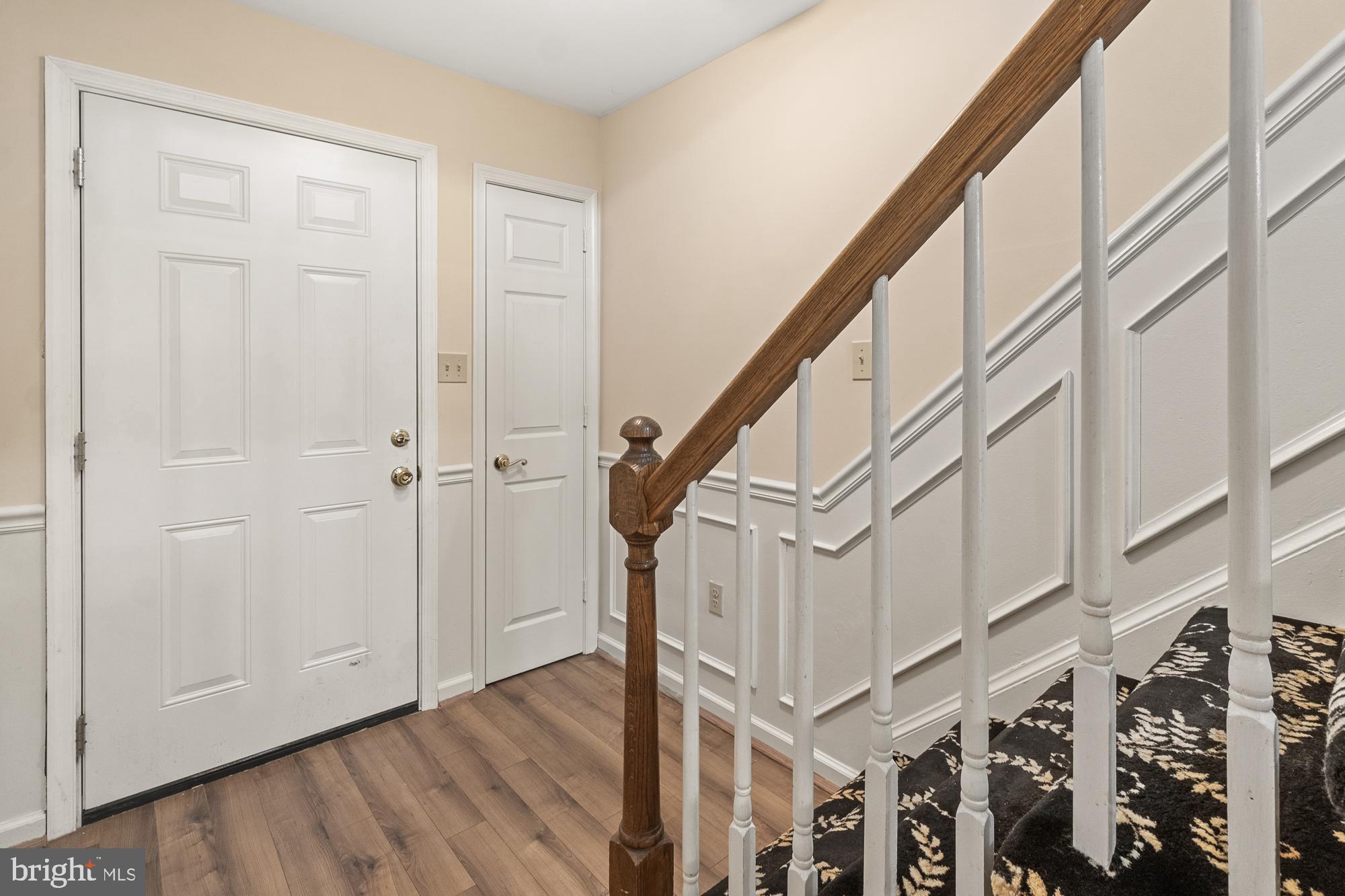 Entryway with two white doors beside a staircase with a dark wood handrail and patterned runner.