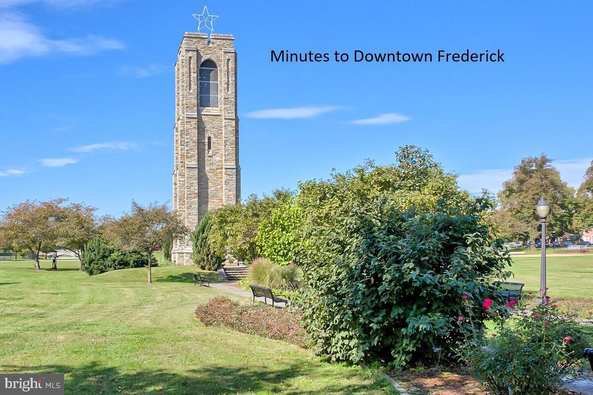 Frederick park with a tall stone tower, benches, and landscaped flower beds.
