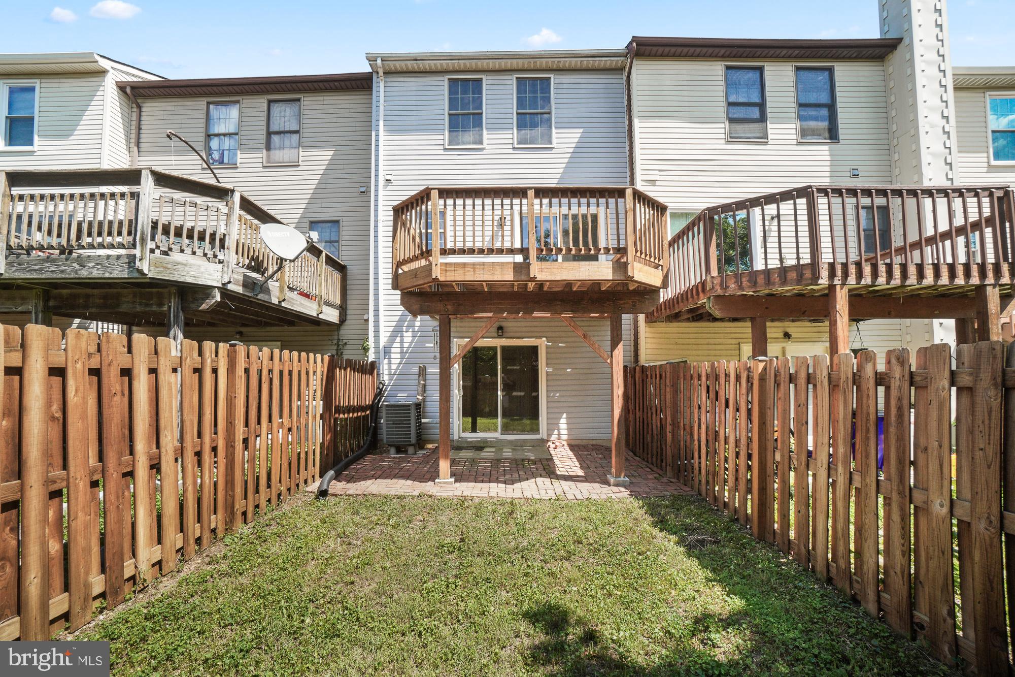 Townhouse rear with a raised wooden deck, fenced grassy yard, and brick patio.