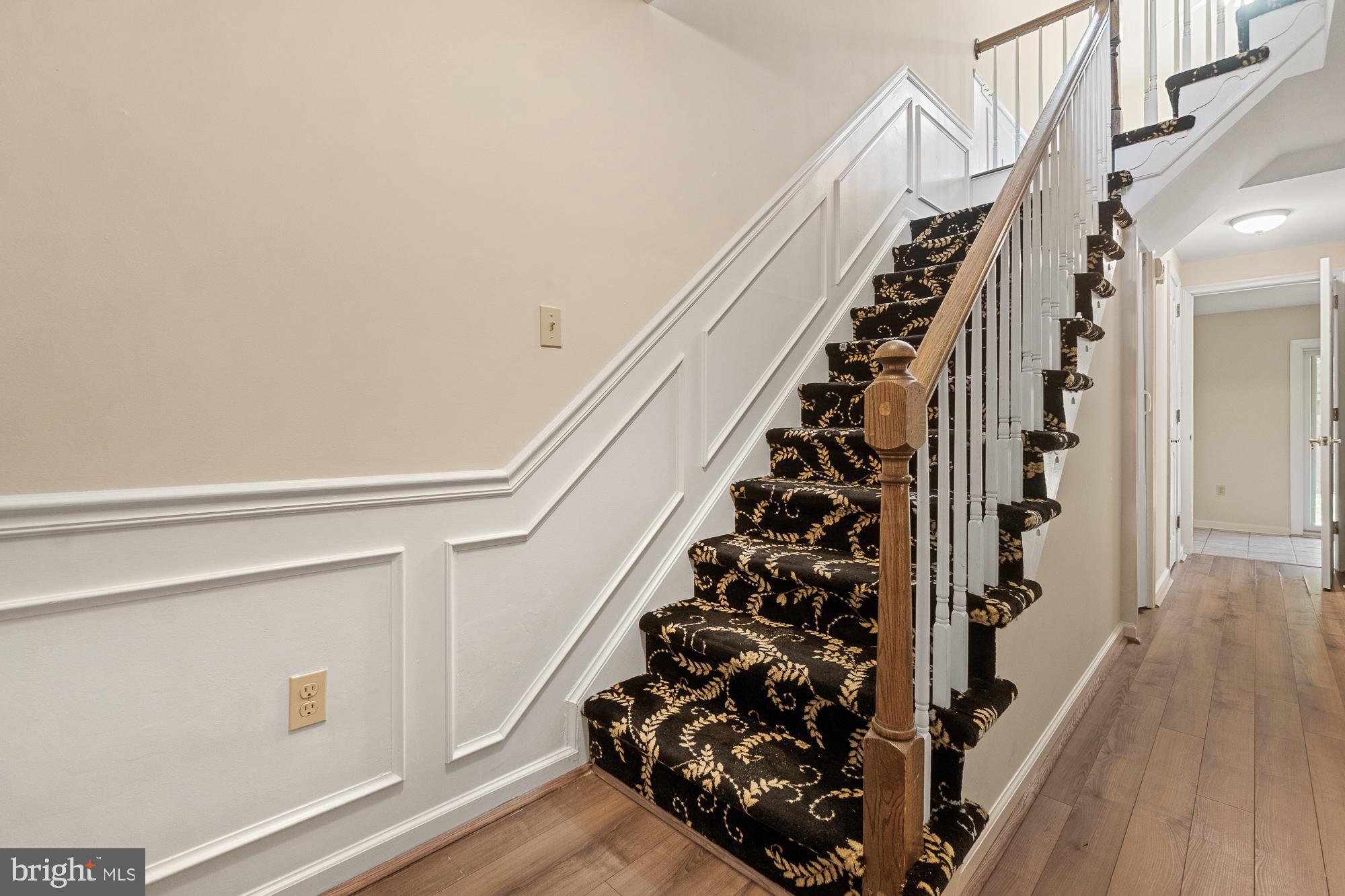 Interior staircase with black-and-gold patterned carpet, white paneling, and a wooden handrail.