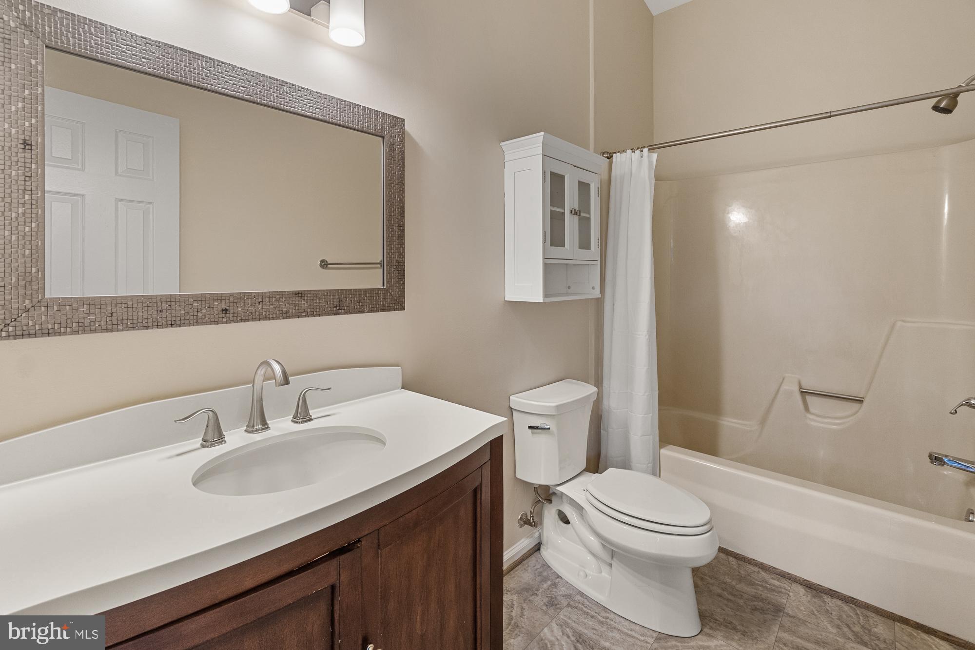 Bathroom with a dark wood vanity, mosaic-framed mirror, toilet, and bathtub behind a white shower curtain.