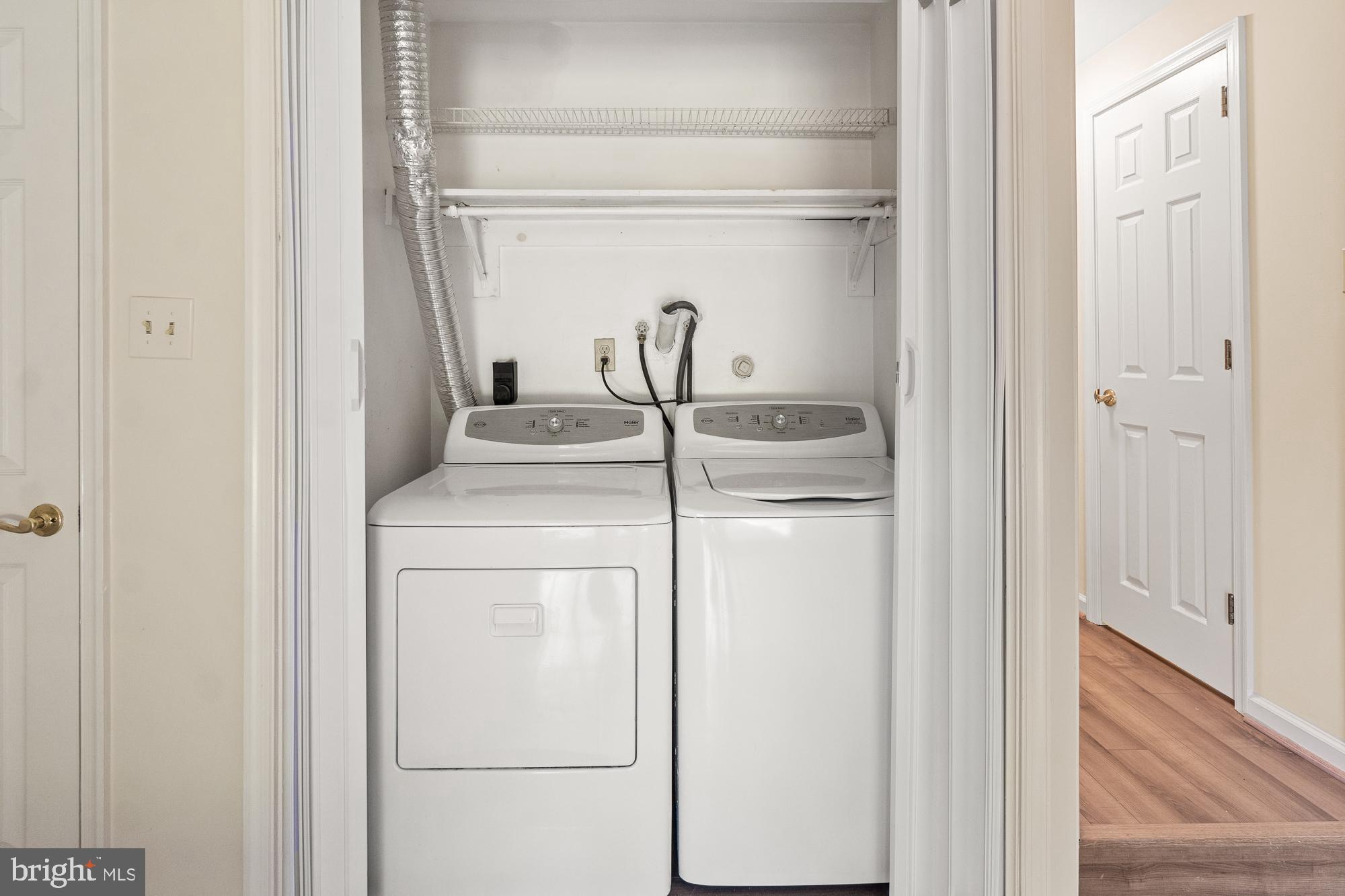 Laundry closet with white washer and dryer beneath an overhead wire shelf.