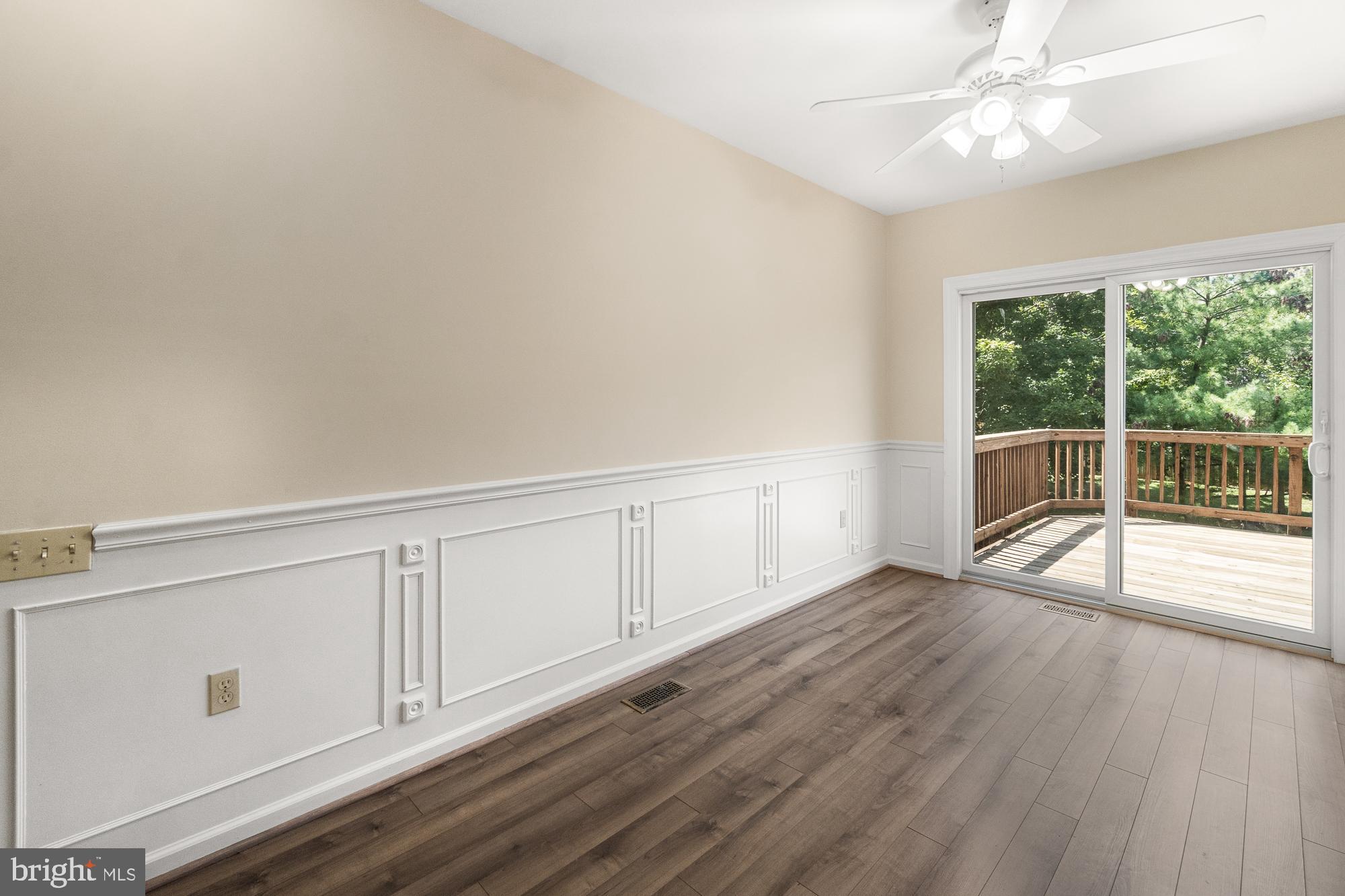 Vacant room with decorative wainscoting and wood floors opening onto a tree-lined deck.