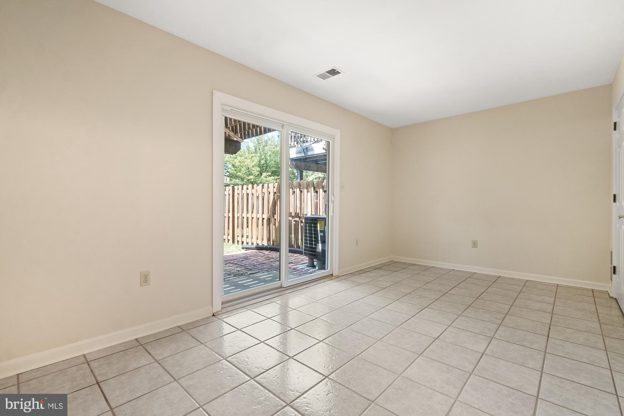 Vacant tiled room with sliding glass doors opening onto a fenced brick patio.