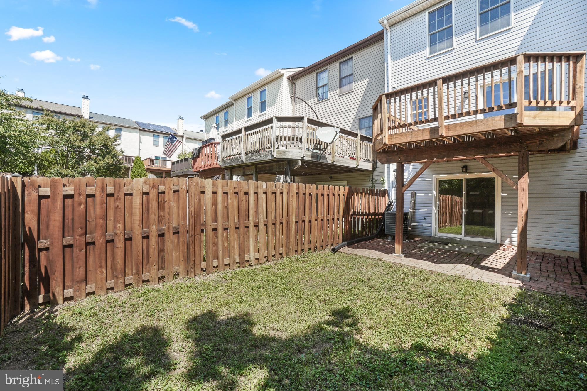 Townhouse backyard with raised wooden decks, a tall privacy fence, and a brick patio.