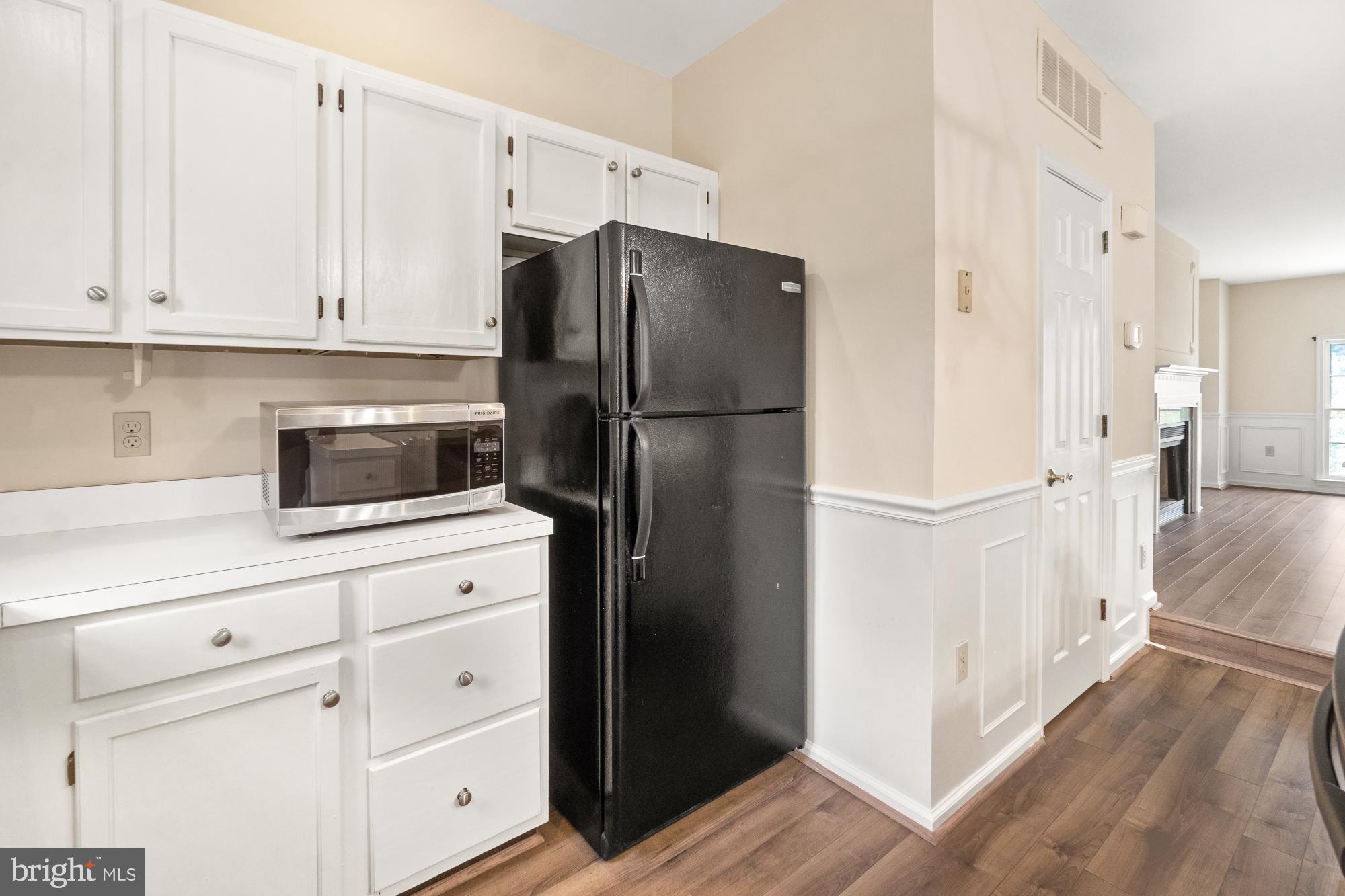 Kitchen with white cabinetry, black refrigerator, stainless-steel microwave, and wood-look flooring.