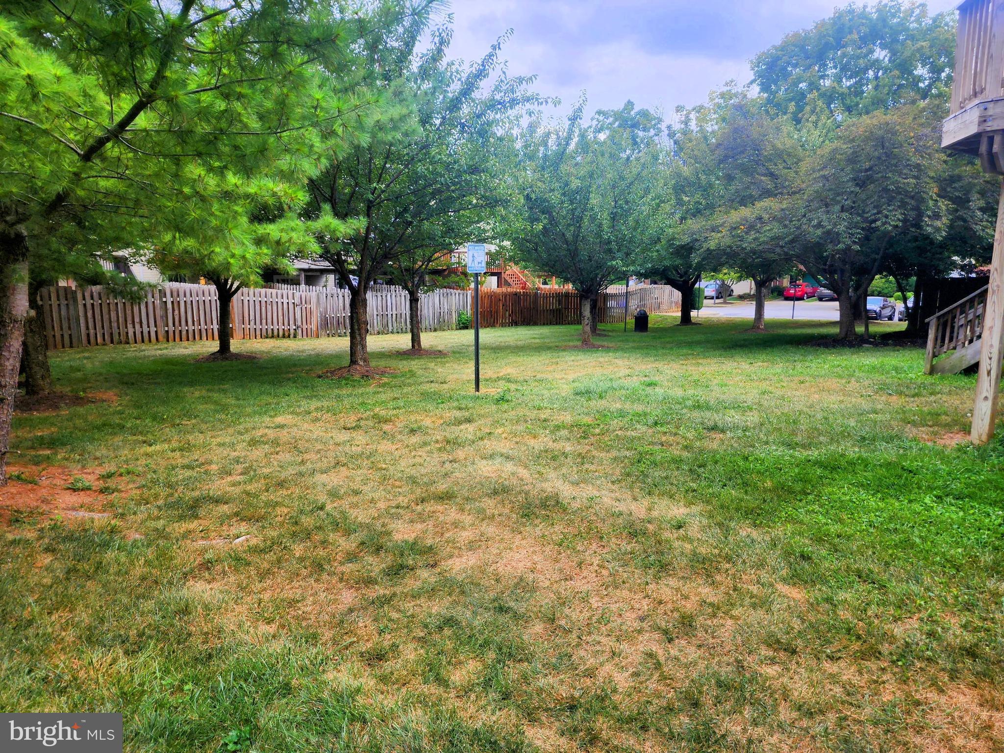 Grassy yard with mature trees, a wooden fence, and a neighboring deck.