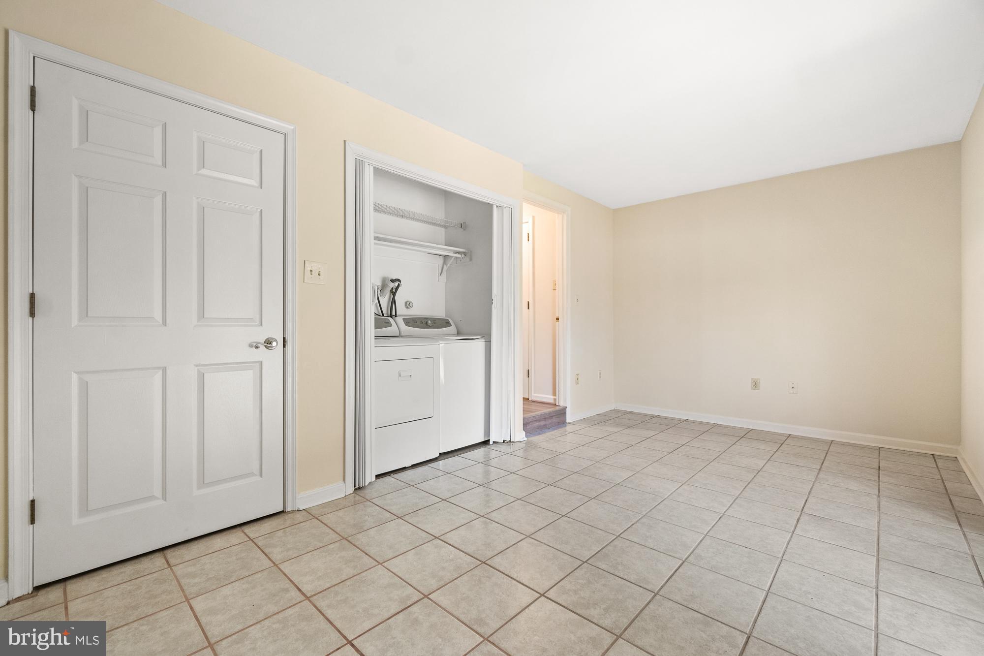 Tiled laundry room with a washer and dryer in a closet and a paneled door.