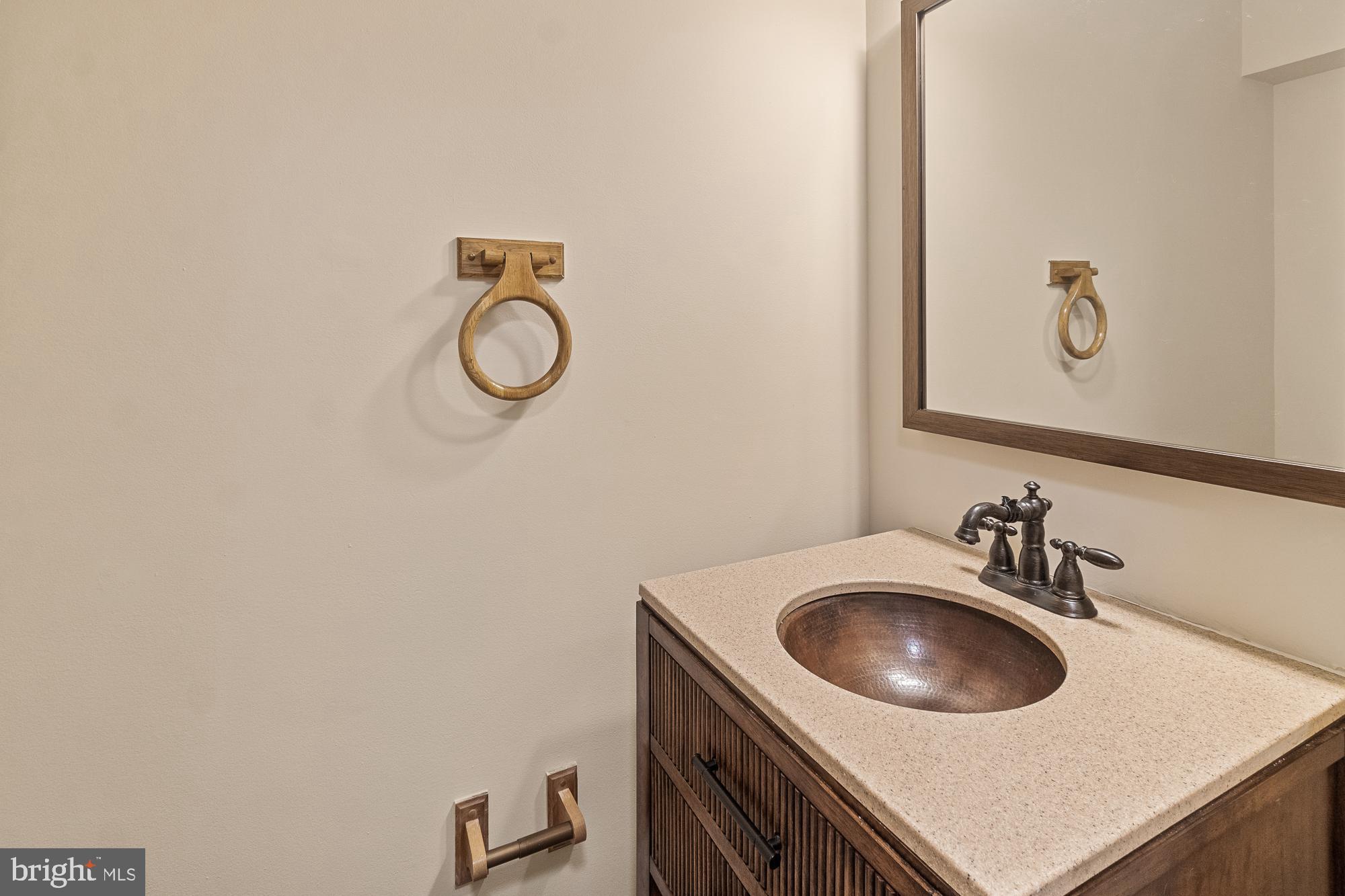 Bathroom vanity with a hammered copper sink, light stone countertop, and dark wood cabinet.