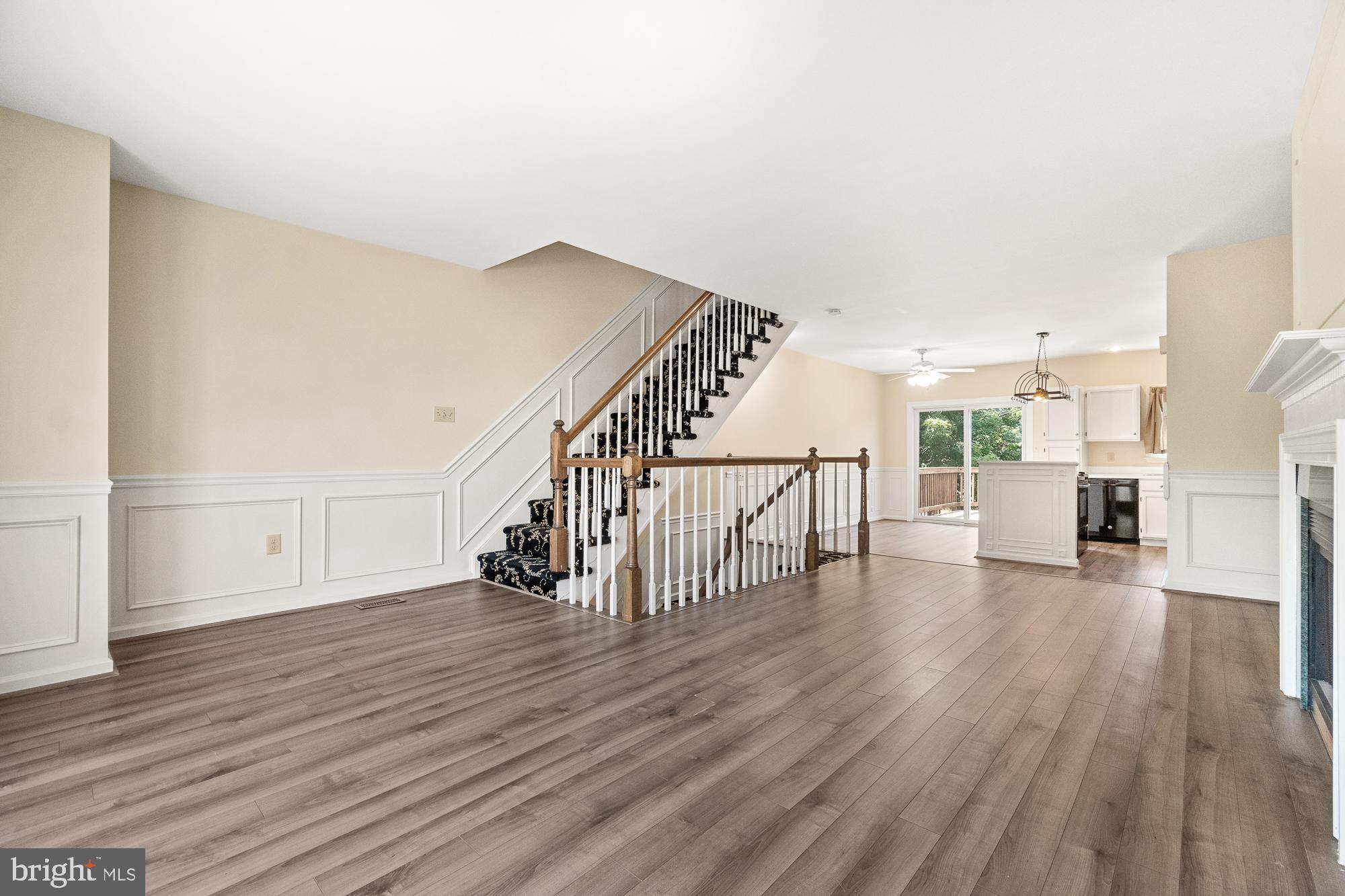 Open-plan living area with wood-look floors, a carpeted staircase, and a white kitchen.