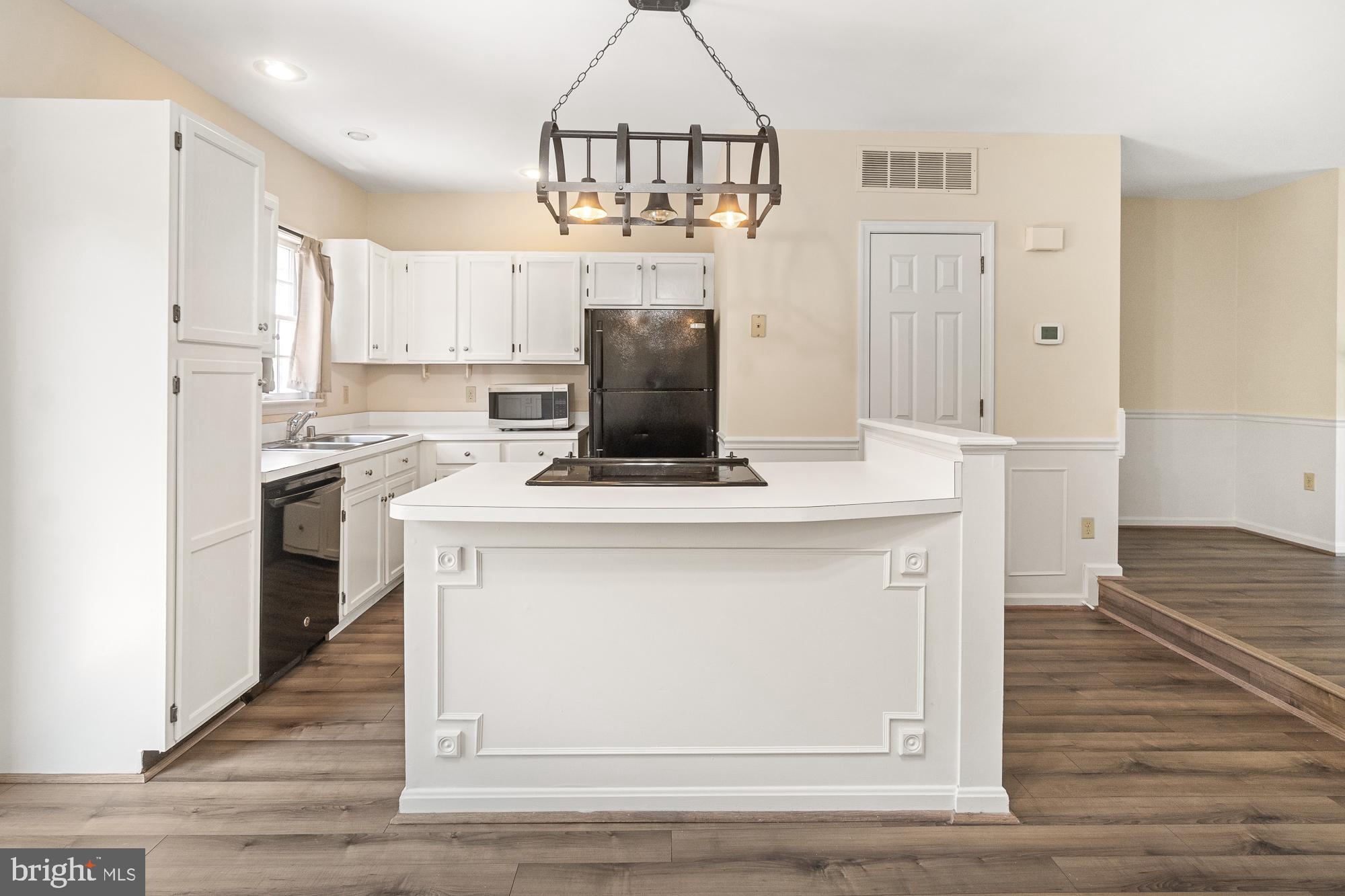 Kitchen with white cabinets, dark appliances, and a large island with a cooktop beneath a metal chandelier.