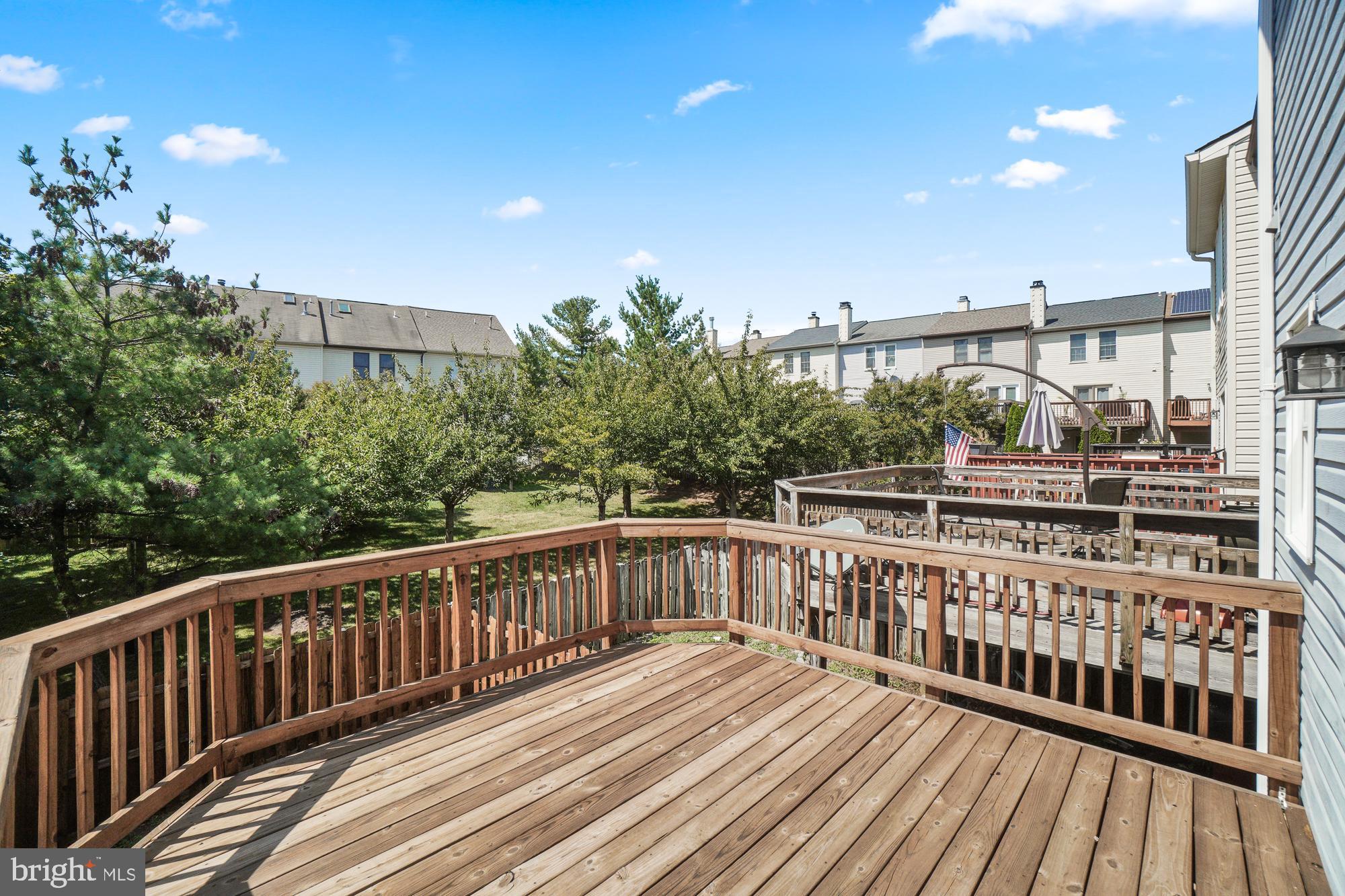 Wooden backyard deck overlooking a leafy shared green space and neighboring townhouses.