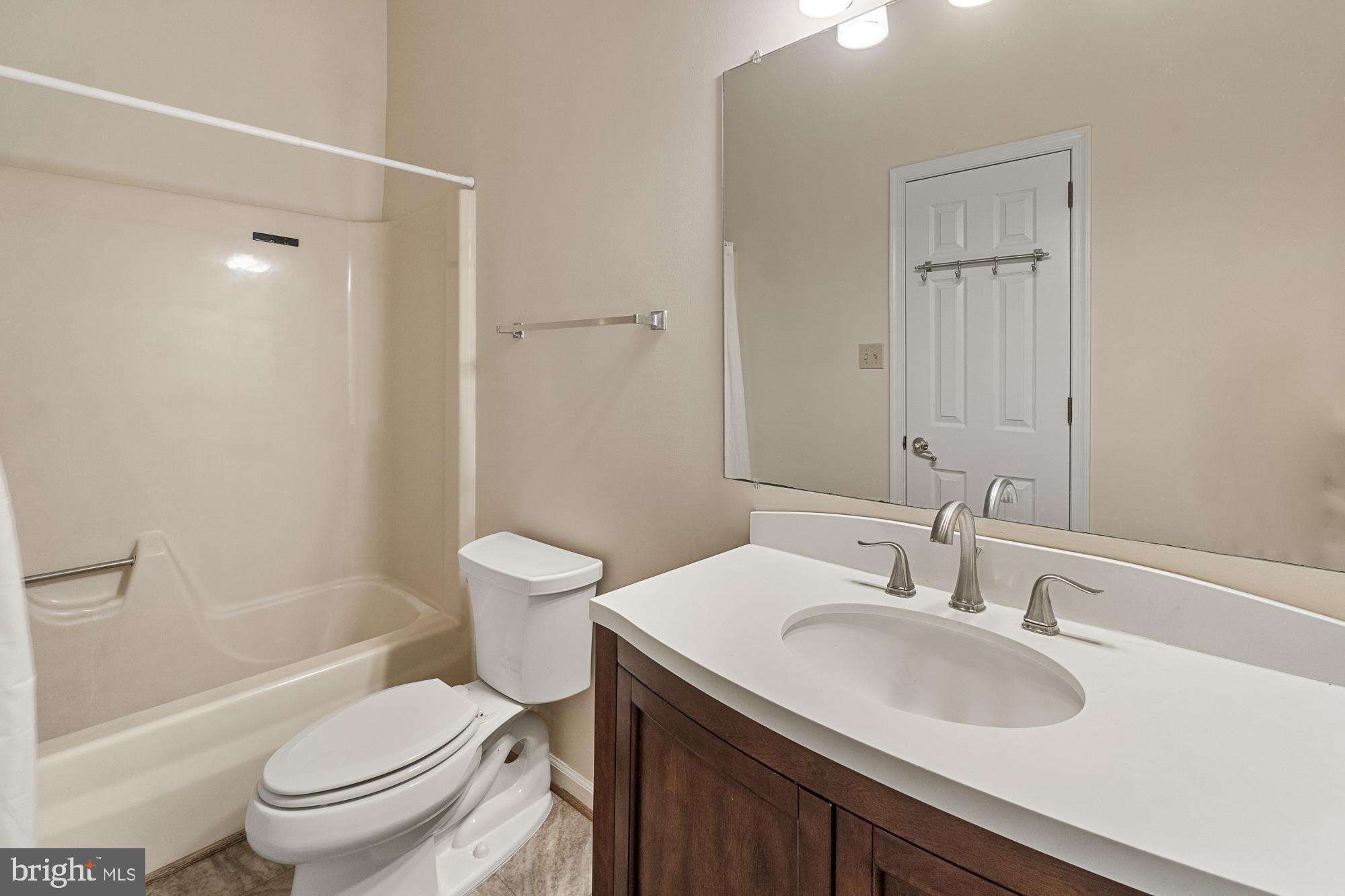 Bathroom with a tub and shower, toilet, and dark wood vanity with a large mirror.