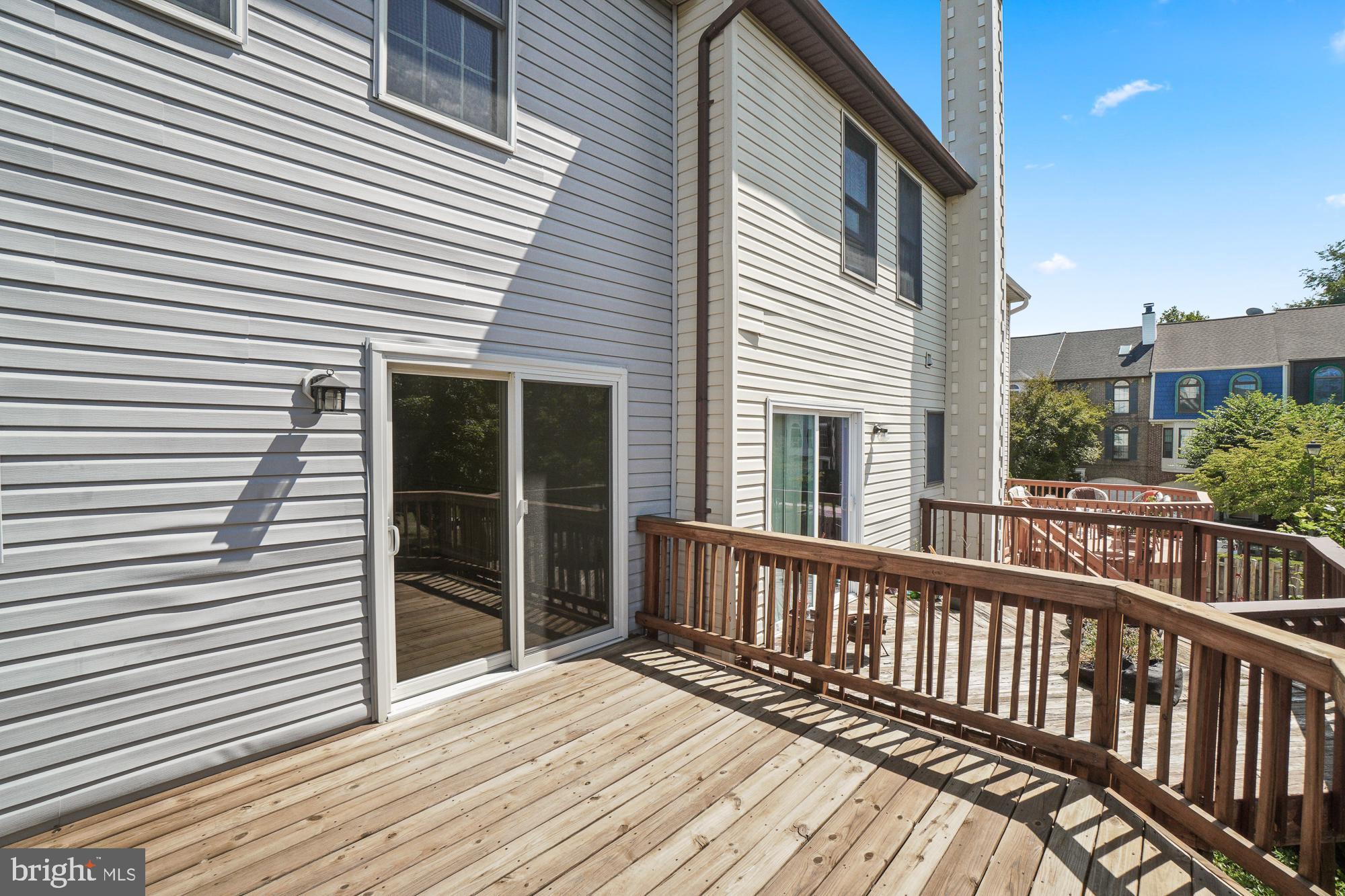 Spacious wooden deck with railing beside a light-sided home and sliding glass doors.