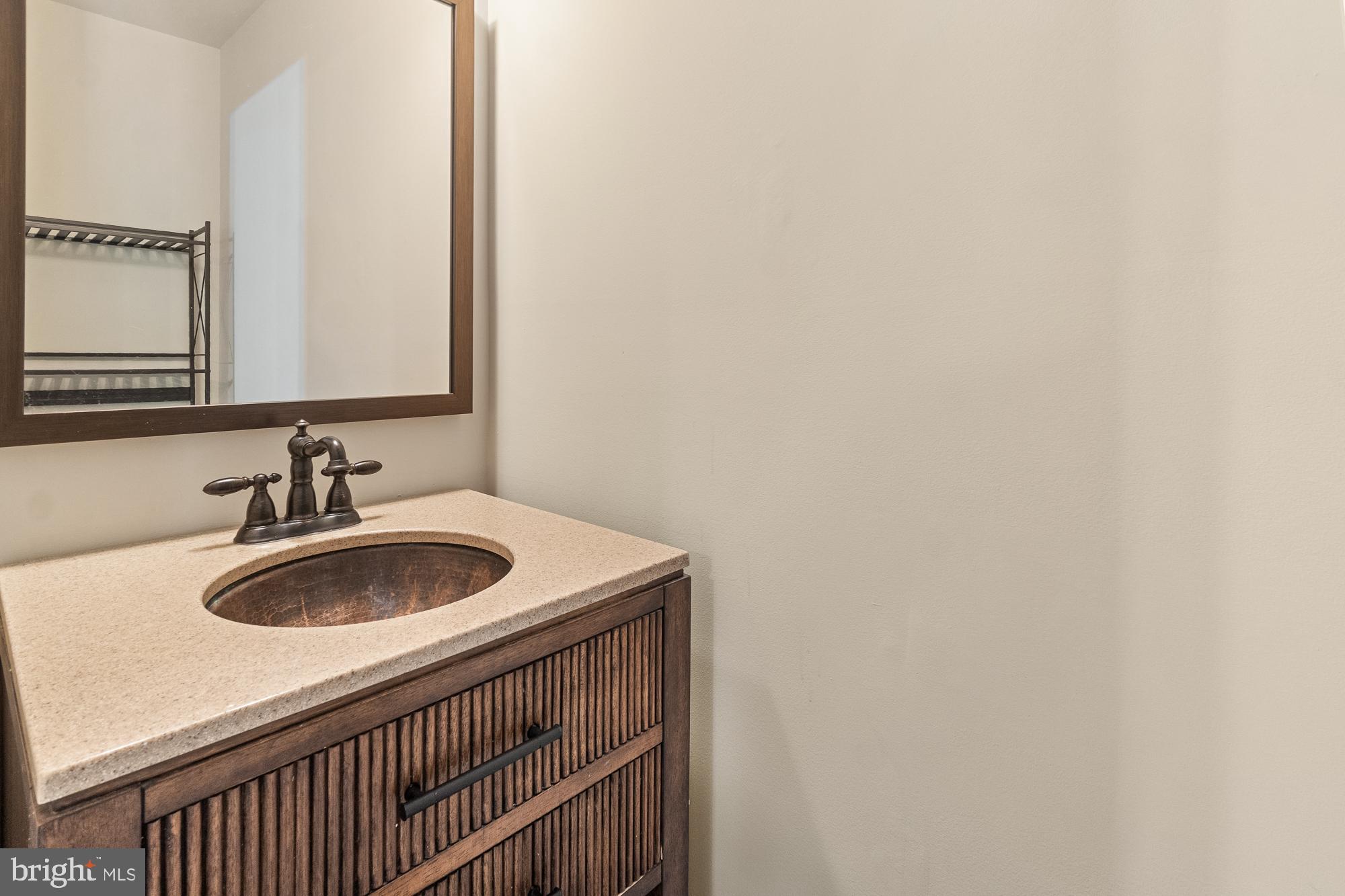 Bathroom vanity with a copper-toned sink, fluted wood cabinet, and large framed mirror.