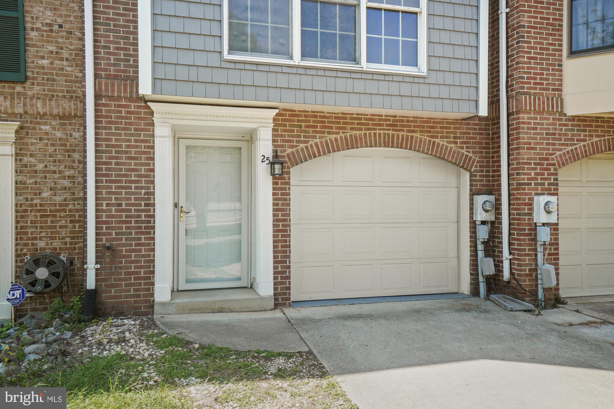 Brick townhouse entrance and arched garage door beneath gray upper-story siding.