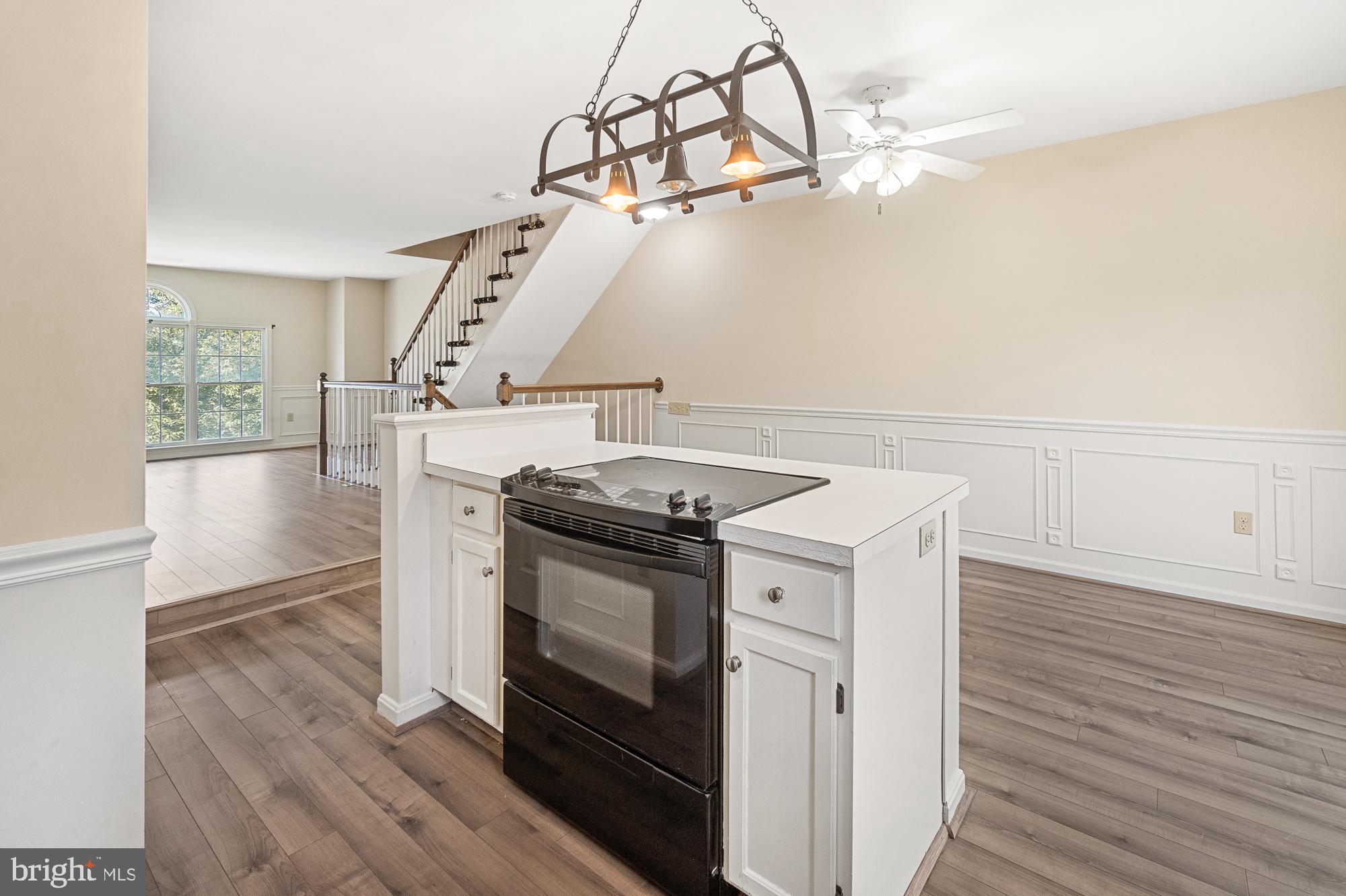 Open kitchen with a white peninsula, black range, wood-look floors, and staircase.