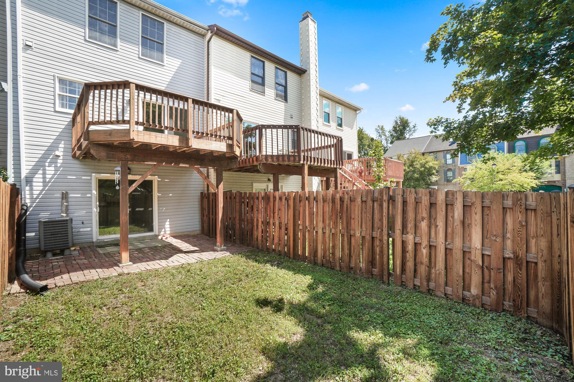 Home’s fenced backyard with raised wooden decks and a brick patio.