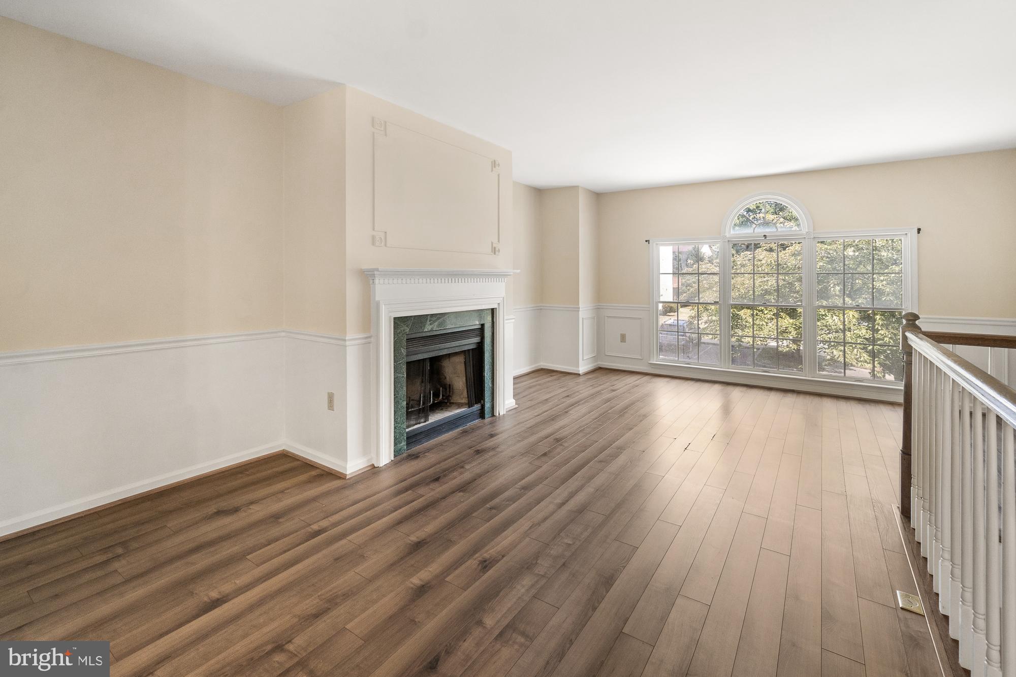 Empty living room with a fireplace, plank flooring, and a large arched window.