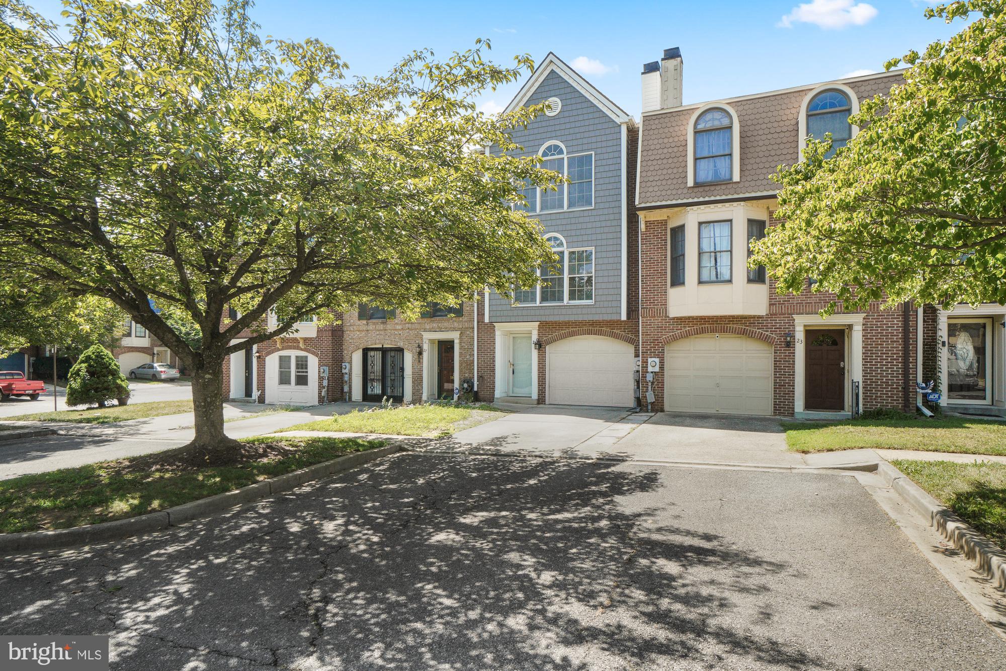 Attached townhouse with blue-gray shingle siding, arched windows, and an attached garage, partly shaded by a leafy tree.