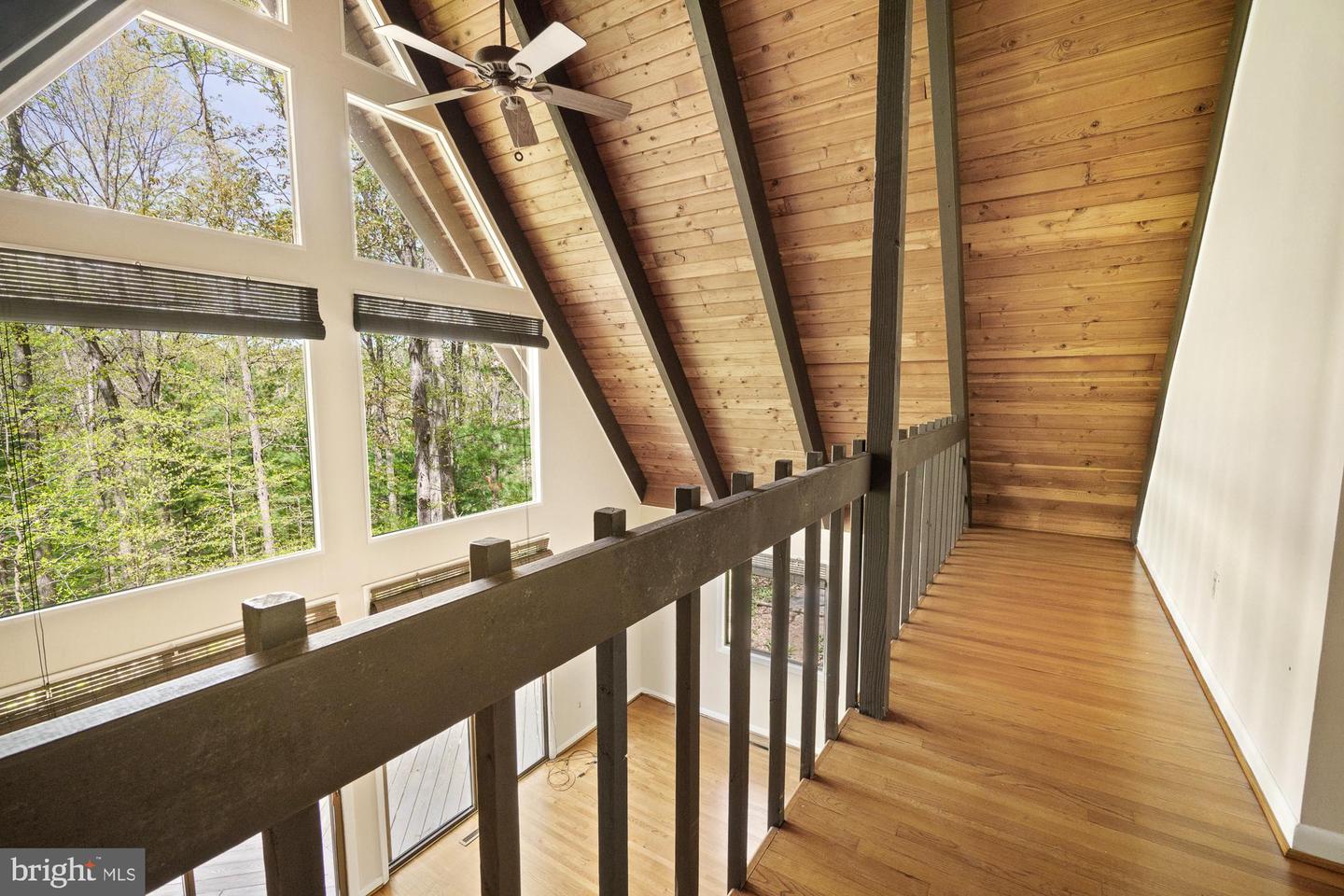 Wood-floored loft walkway beneath a vaulted timber ceiling, with large windows overlooking trees.