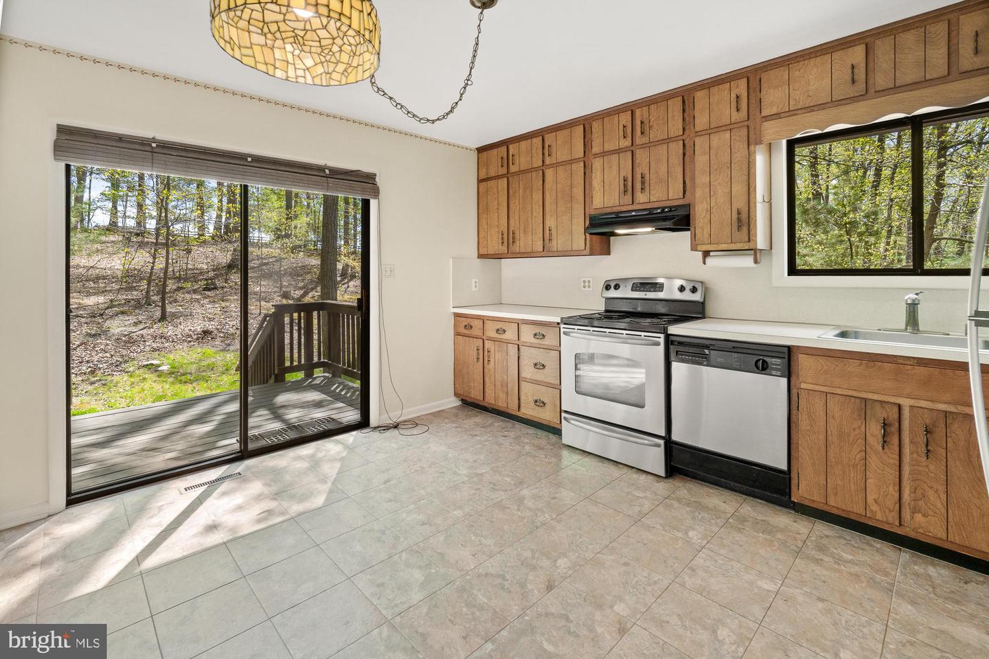 Kitchen with wood cabinetry and stainless steel appliances beside a sliding door to a wooded deck.