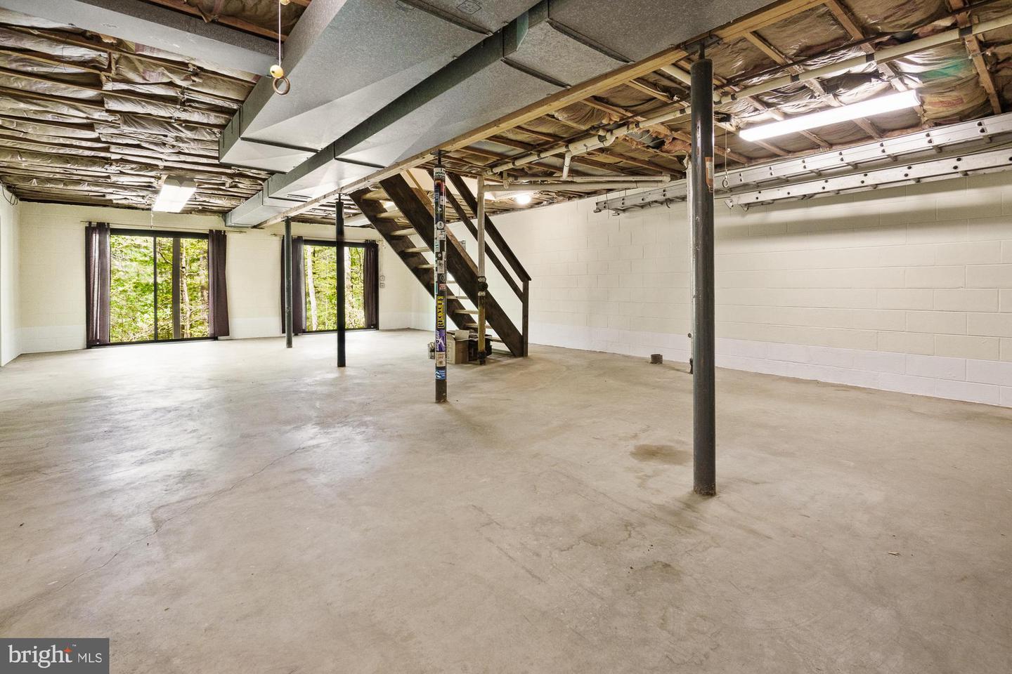 Unfinished basement with a concrete floor, exposed ceiling, support posts, and wooden stairs.