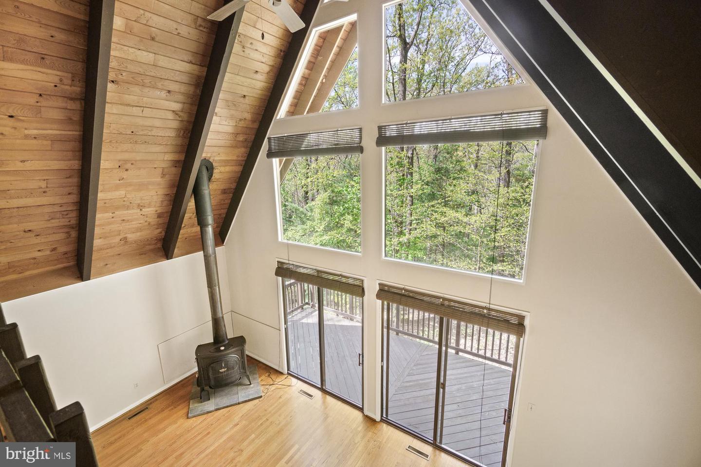 Vaulted living room with a wood-burning stove, tall windows, and glass doors to a wooded deck.