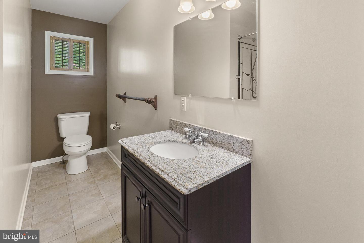 Bathroom with a granite vanity, dark cabinetry, tiled floor, and shuttered window.