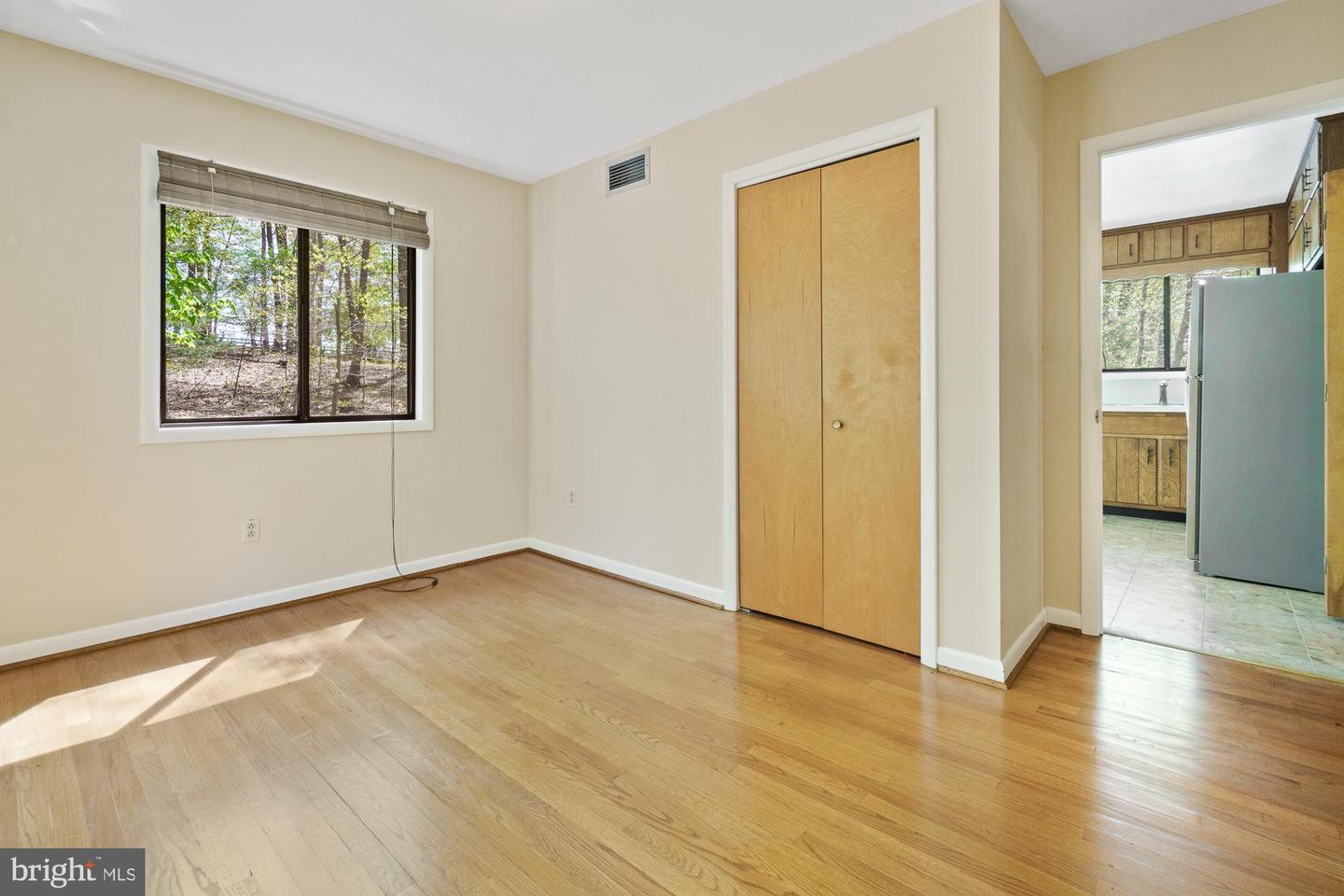 Empty bedroom with hardwood floors, a wooded view, and a doorway to the kitchen.