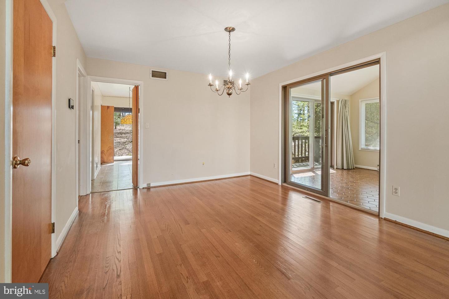 Empty dining room with hardwood floors, a chandelier, and sliding glass doors to a tiled sunroom.