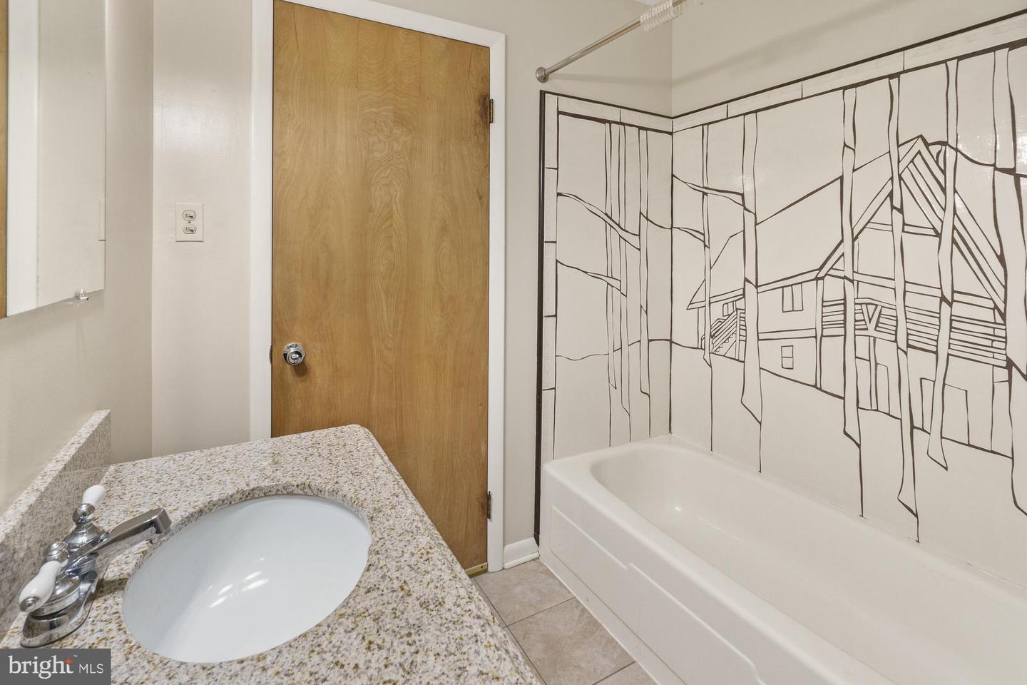 Bathroom with a bathtub featuring a black line-art surround and a granite vanity.