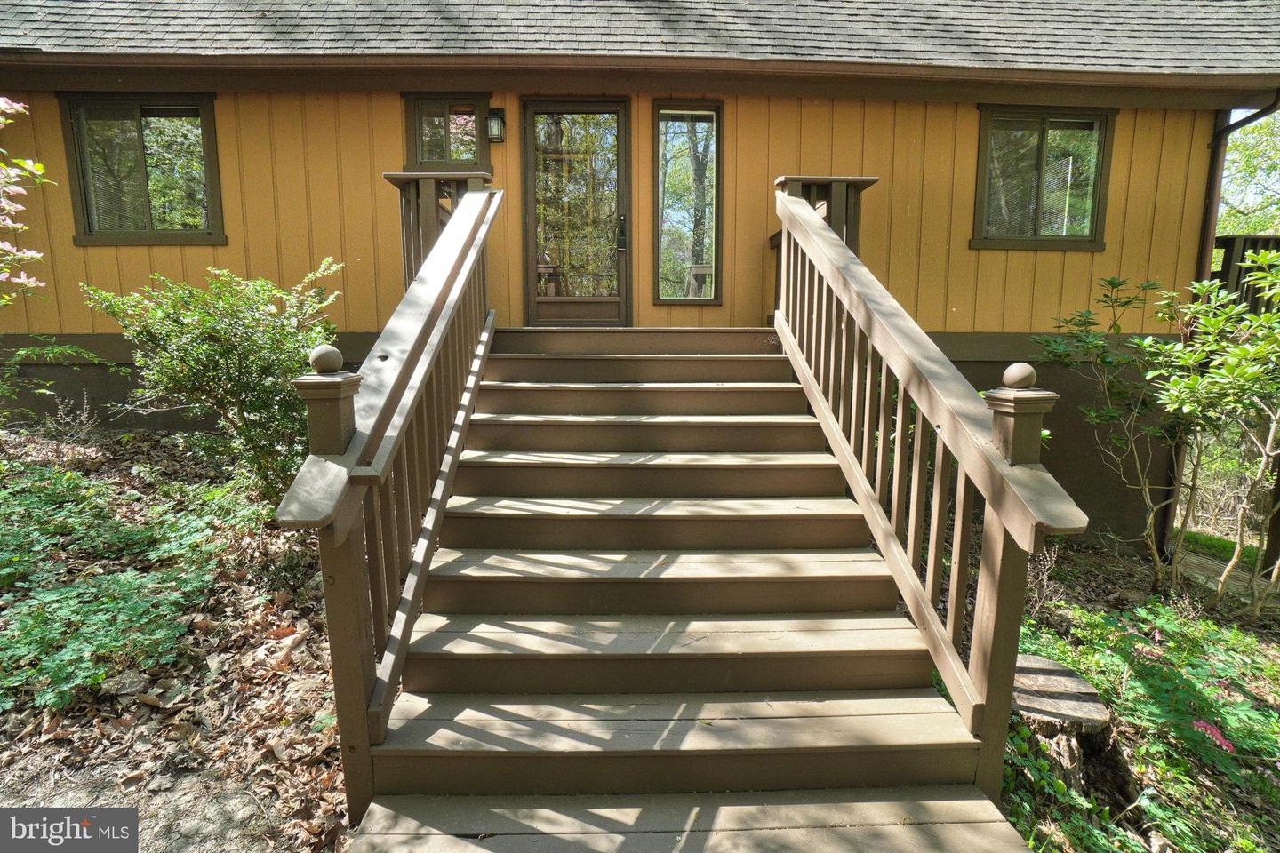Home entrance with broad wooden stairs and railings leading to a glass-paneled door.