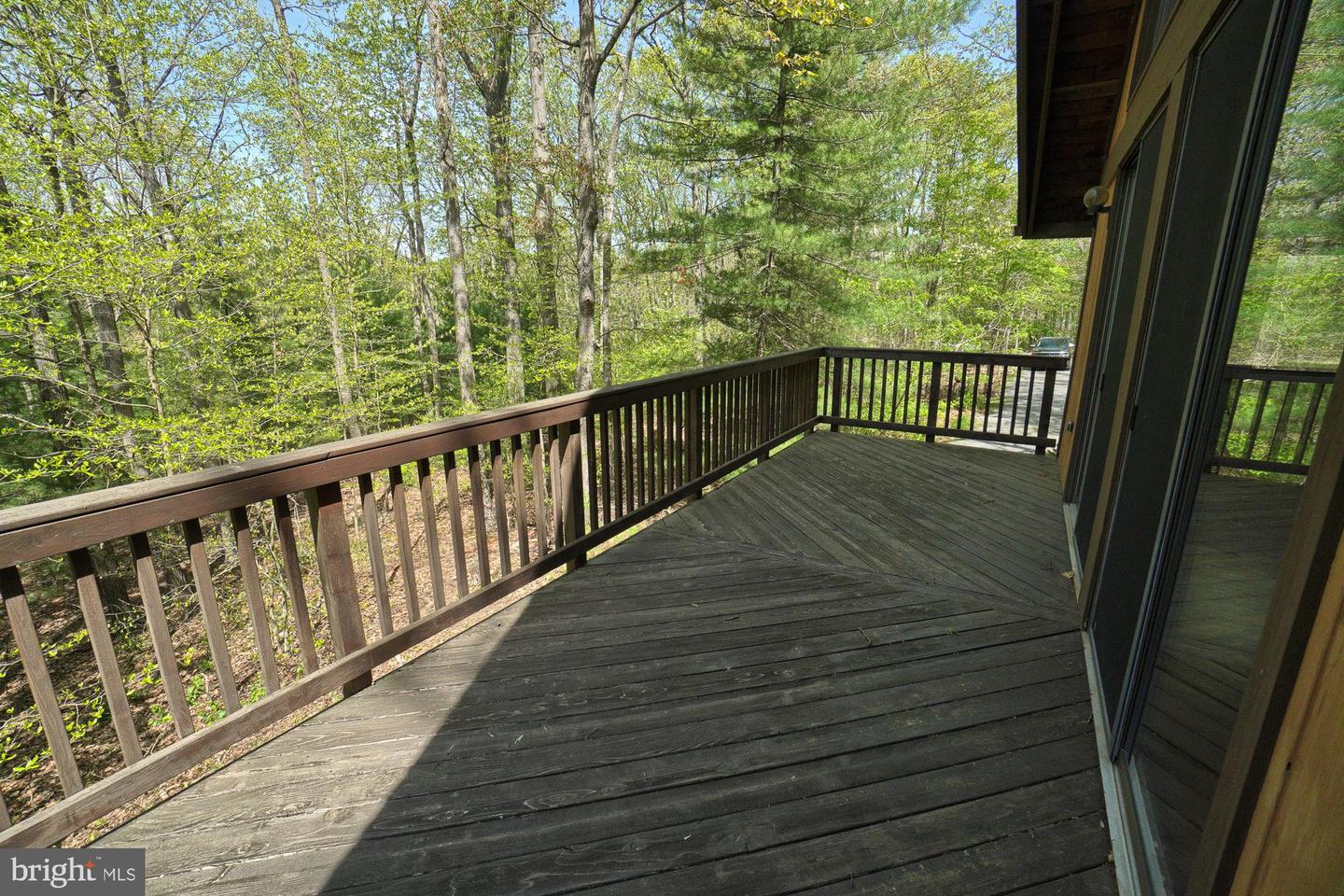 Wooden deck overlooking leafy woods, with dark railings and sliding glass doors.