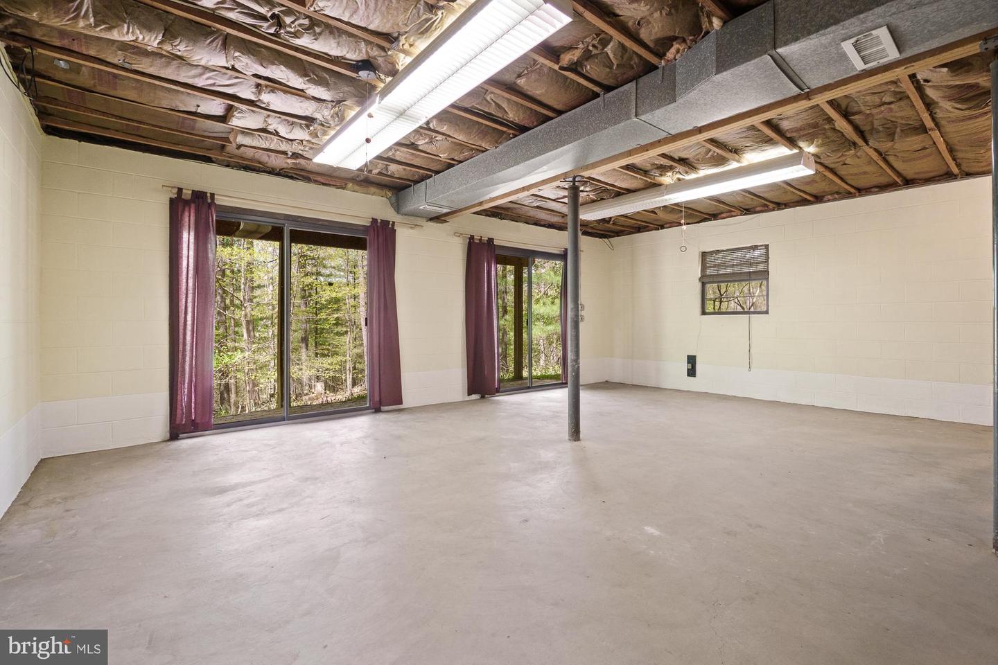 Unfinished basement with exposed ceiling insulation, concrete floor, and sliding glass doors overlooking trees.