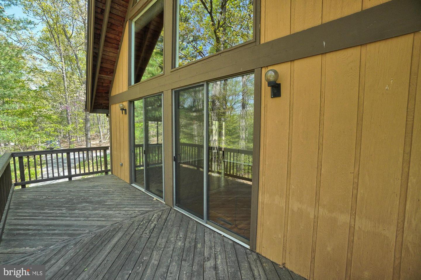 Wooden deck beside a yellow-sided home, with sliding glass doors and a wooded view.