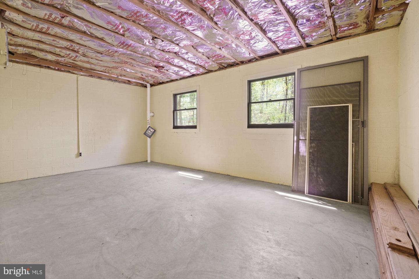 Empty unfinished garage with a concrete floor, exposed ceiling insulation, and screen doors leaning by the windows.