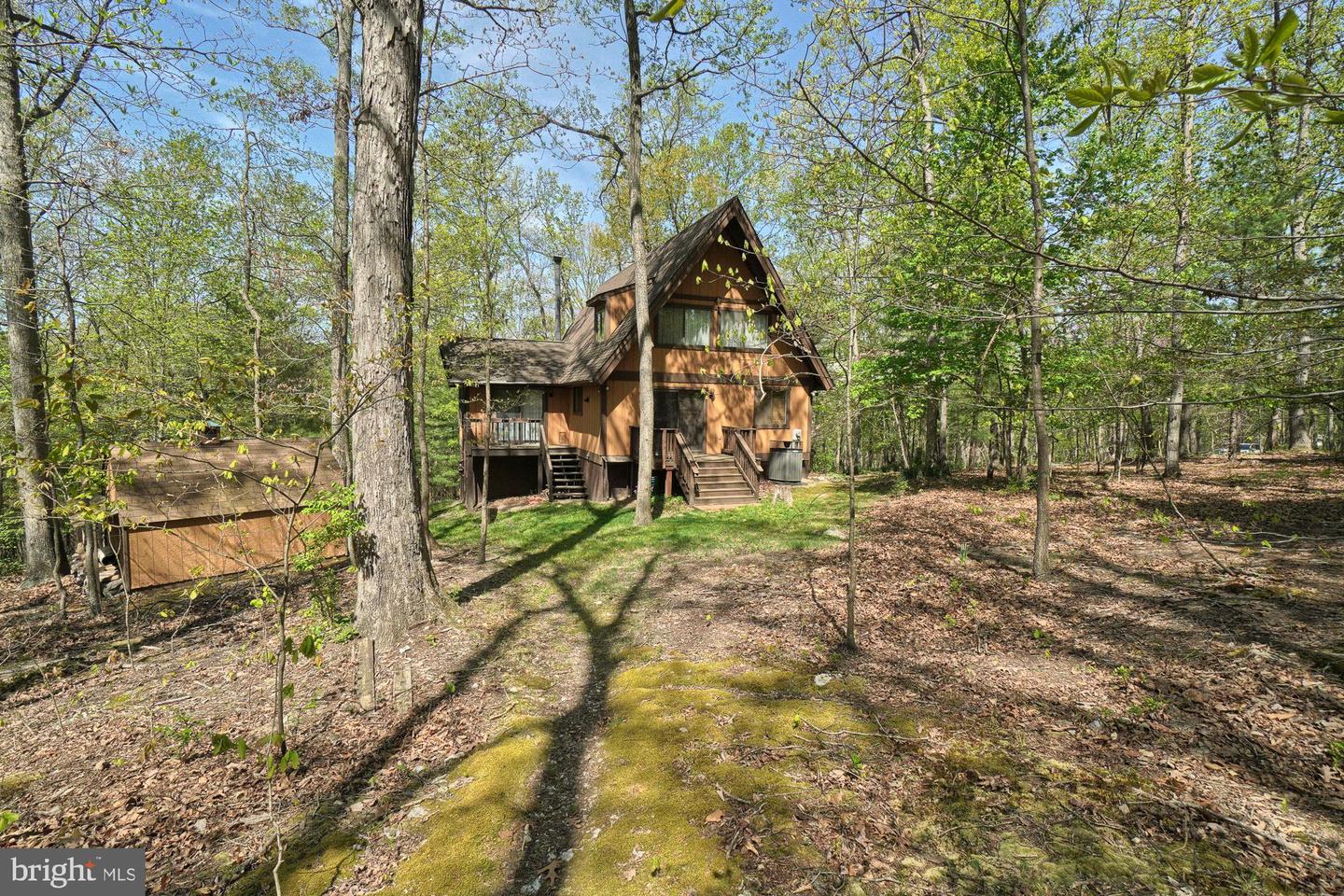 Brown A-frame house with raised decks and a moss-covered path in a wooded lot.