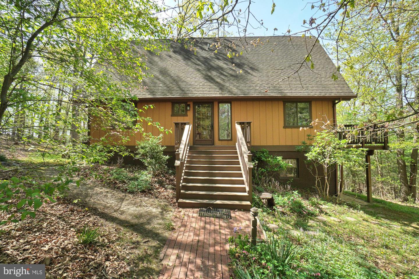 Brown-sided house among trees, with a central staircase and brick walkway to the entrance.