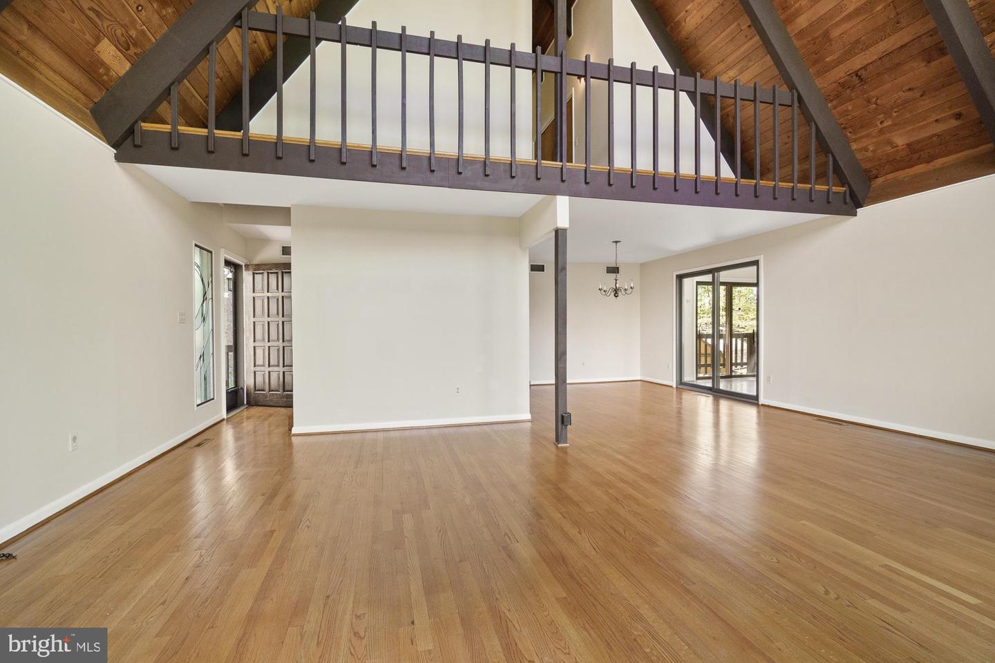 Open living area with hardwood floors, vaulted wood ceiling, and an upper loft with dark railing.