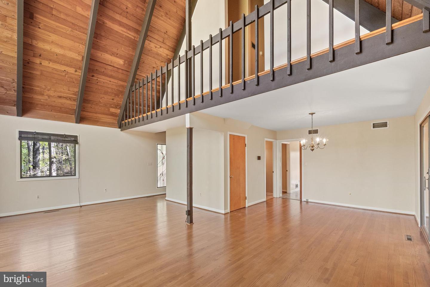 Empty living room with vaulted wood ceiling, loft railing, and hardwood floors.