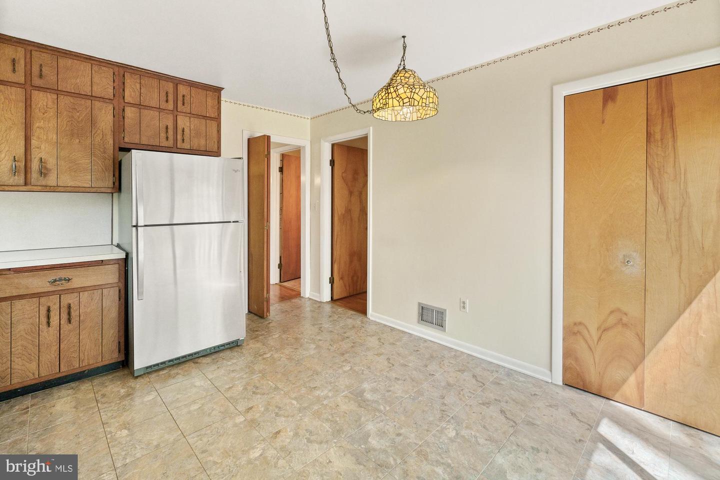 Vacant kitchen with wood cabinets, a white refrigerator, tiled flooring, and a stained-glass pendant light.