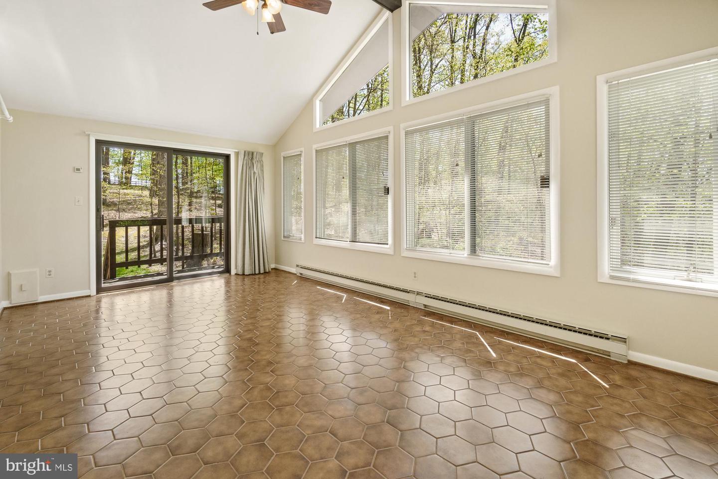 Sunroom with brown hexagonal tile, vaulted ceiling, and large windows overlooking trees.